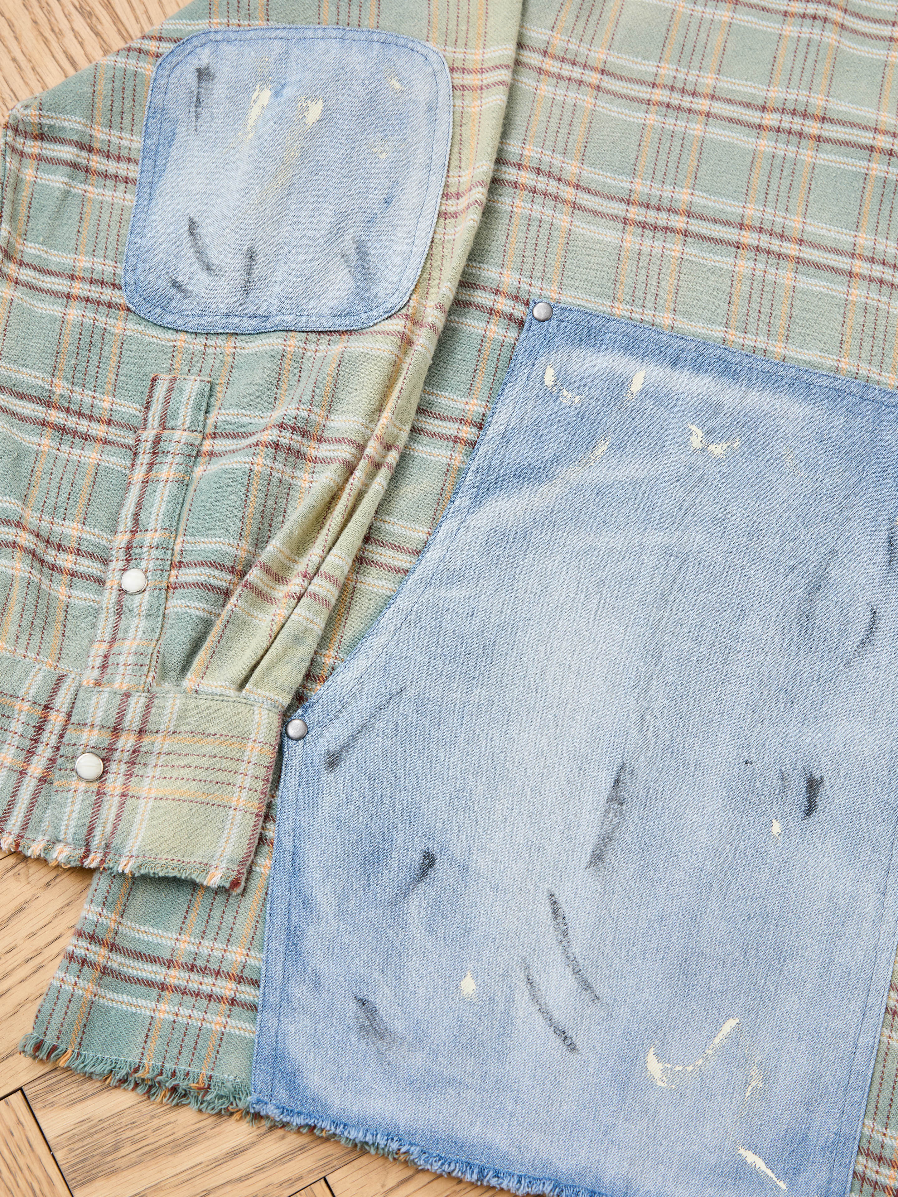 The FOUND Plaid Denim Shirt features green plaid fabric with light denim carpenter pockets on the shoulder and front, both with distressed marks and frayed edges, shown laid flat in a unisex relaxed fit.