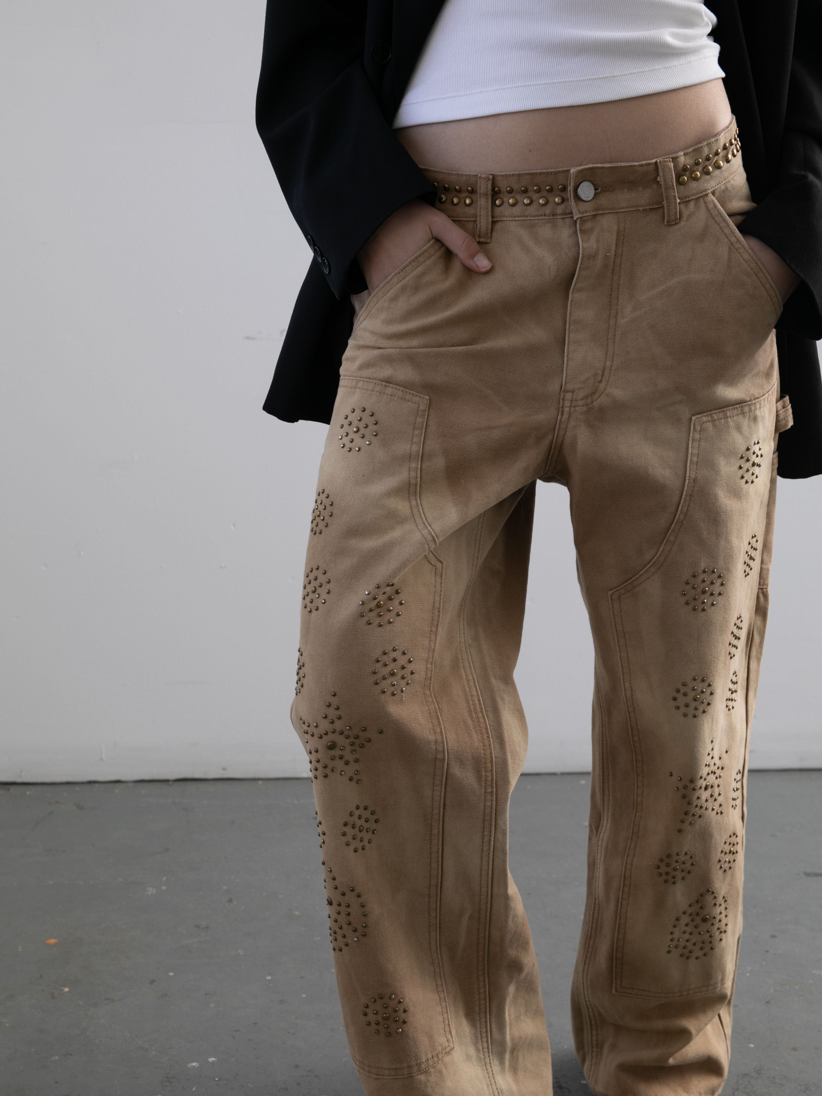 A person in FOUND Canvas Studded Work Pants, a white top, and a black blazer stands against a plain background.