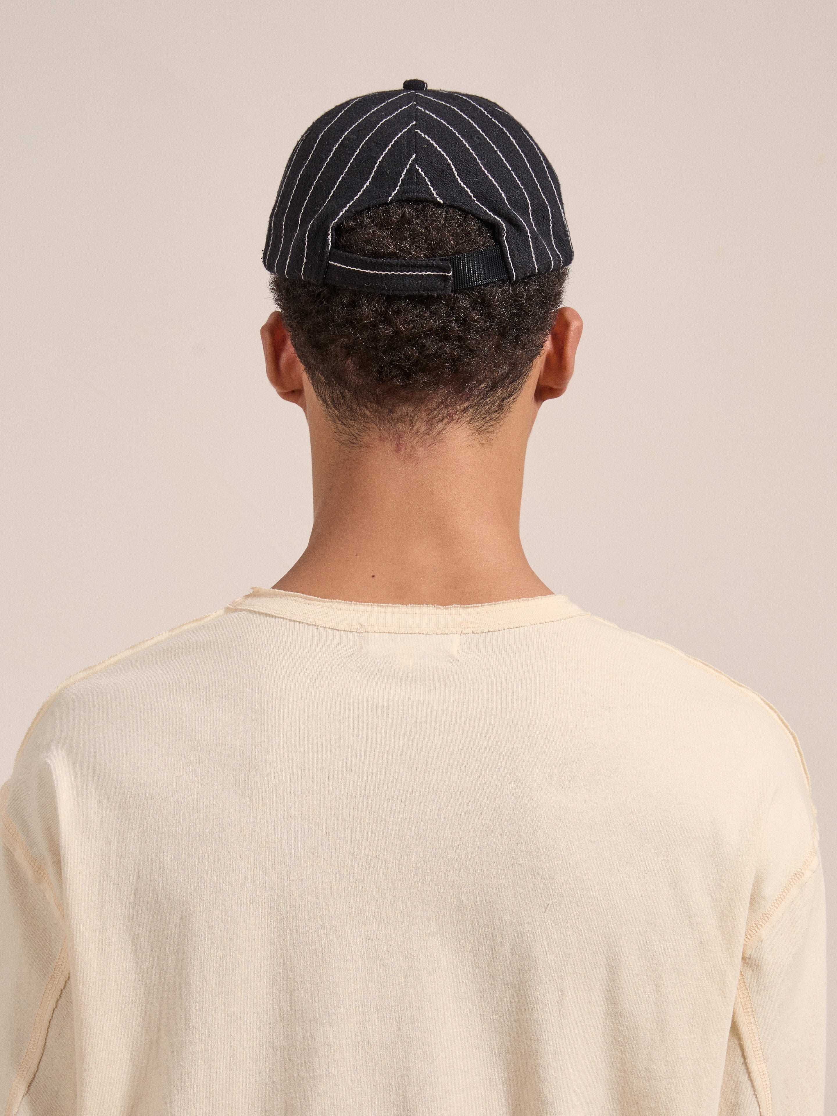 Rear view of a person wearing a light-colored shirt and the FOUND Pinstripe Lion Cap.