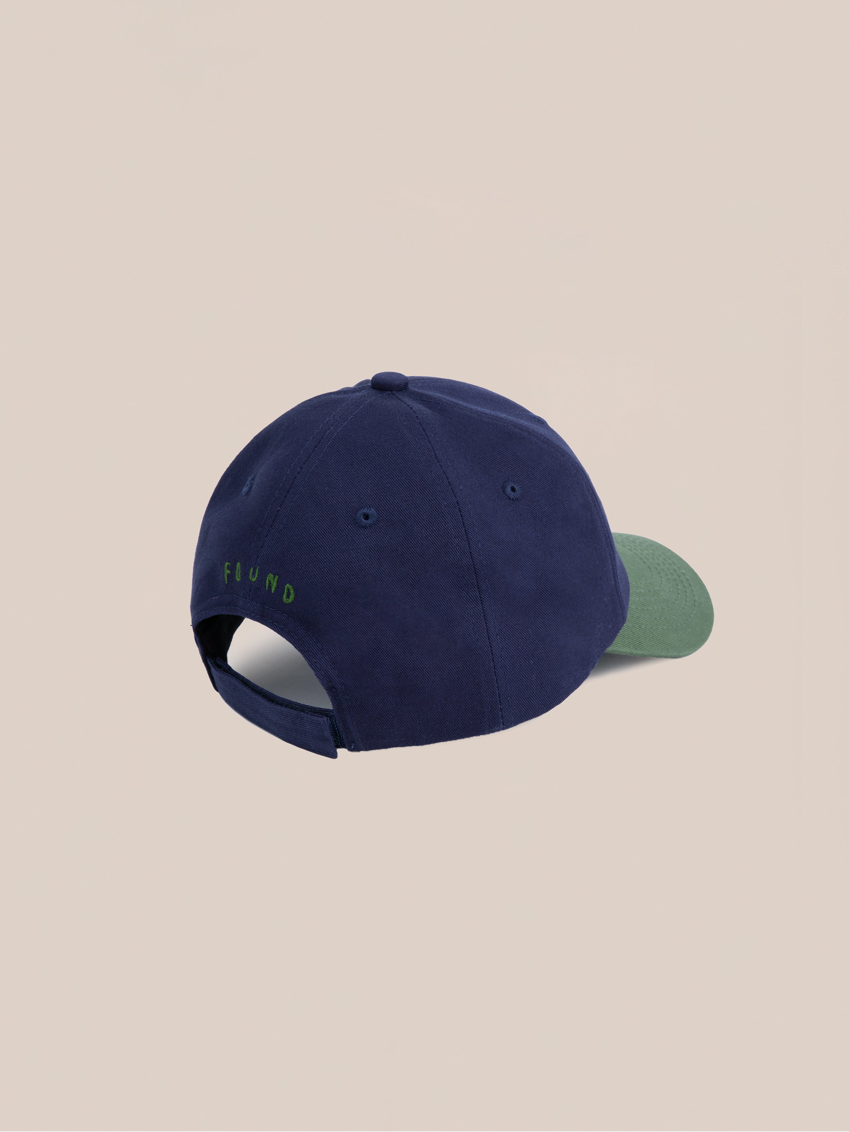 The Horse Equine Cap by Found is a navy baseball cap with a green brim, inspired by 70's color-blocking. It features an adjustable strap and green embroidered text at the back, embodying classic racing hues.