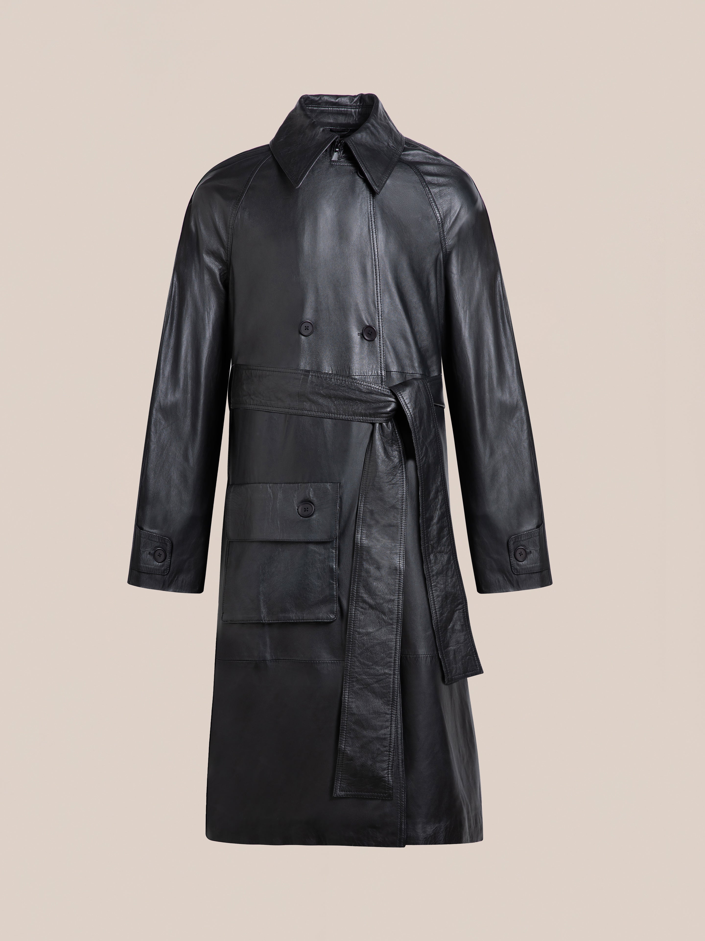 The FOUND Leather Trench Coat, made from premium black leather with double-breasted buttons, a belt, large front pocket, and classic collar, is shown against a plain beige background.