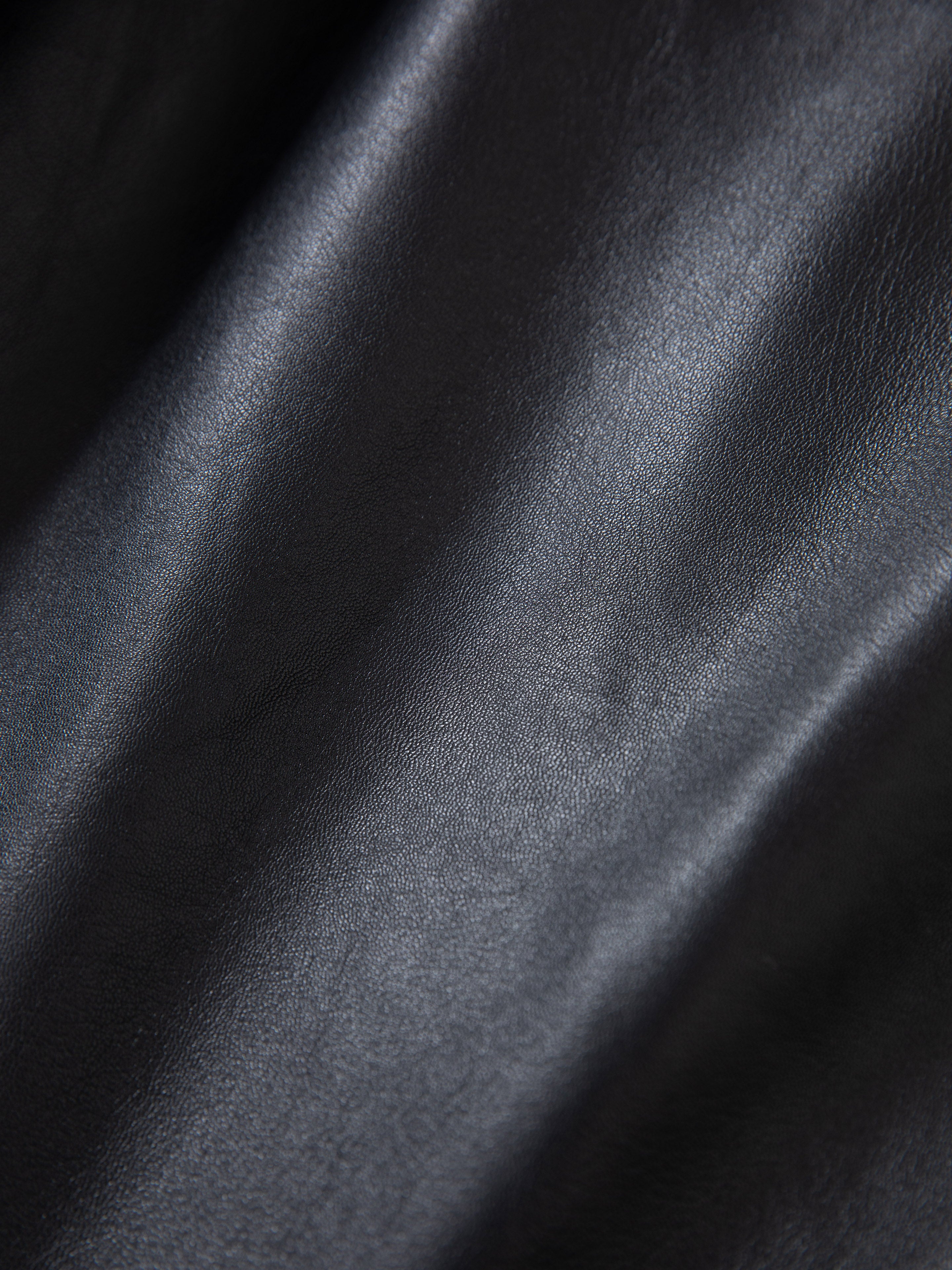 Close-up of FOUND's Leather Trench Coat, showcasing ethically crafted black leather with rich texture and subtle light reflections—perfect for a unisex style.
