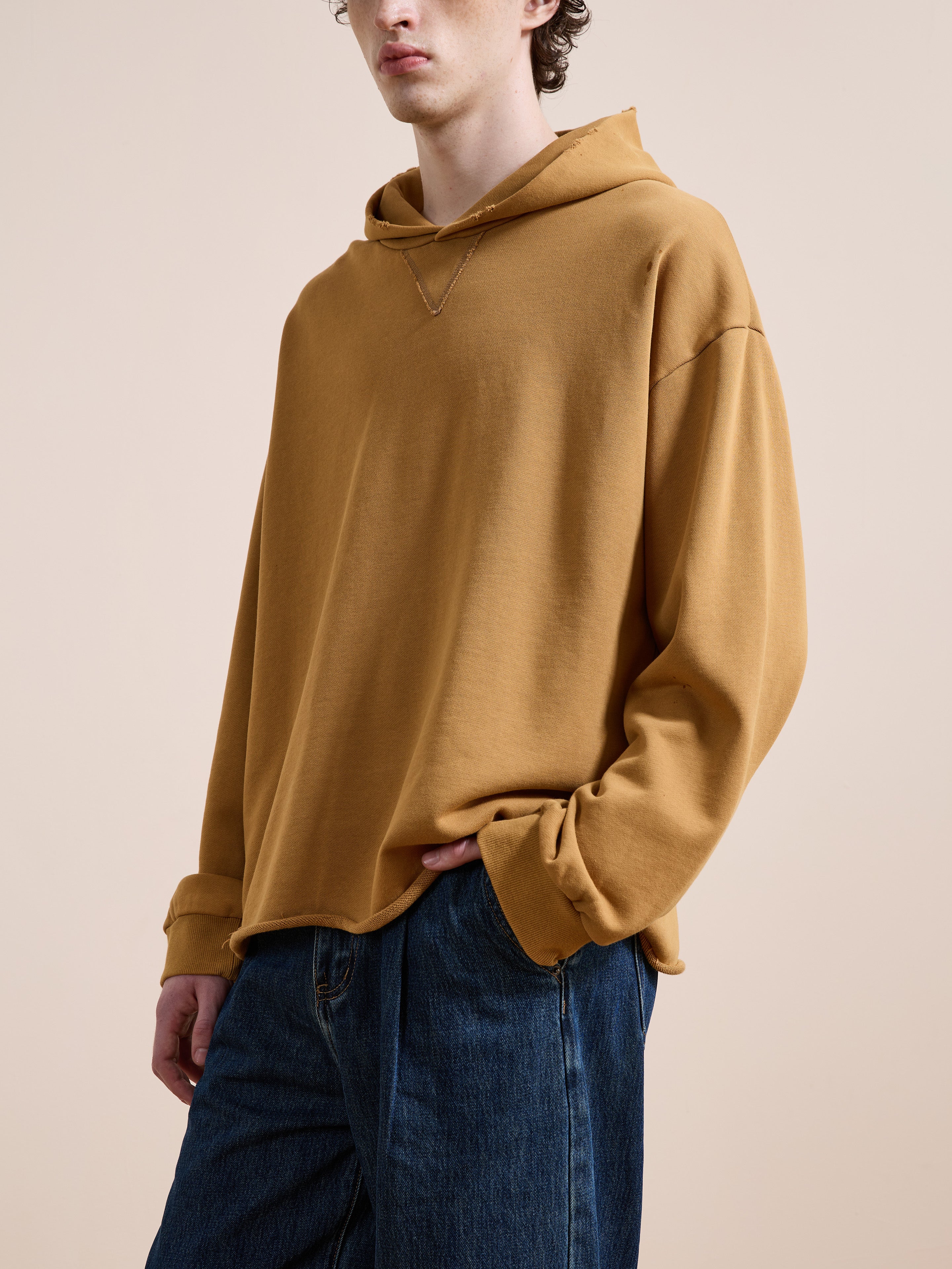 A person in the FOUND Beadwork Logo Hoodie—a loose-fitting, mustard yellow vintage piece made from French terry cotton—paired with blue jeans, stands against a neutral background.