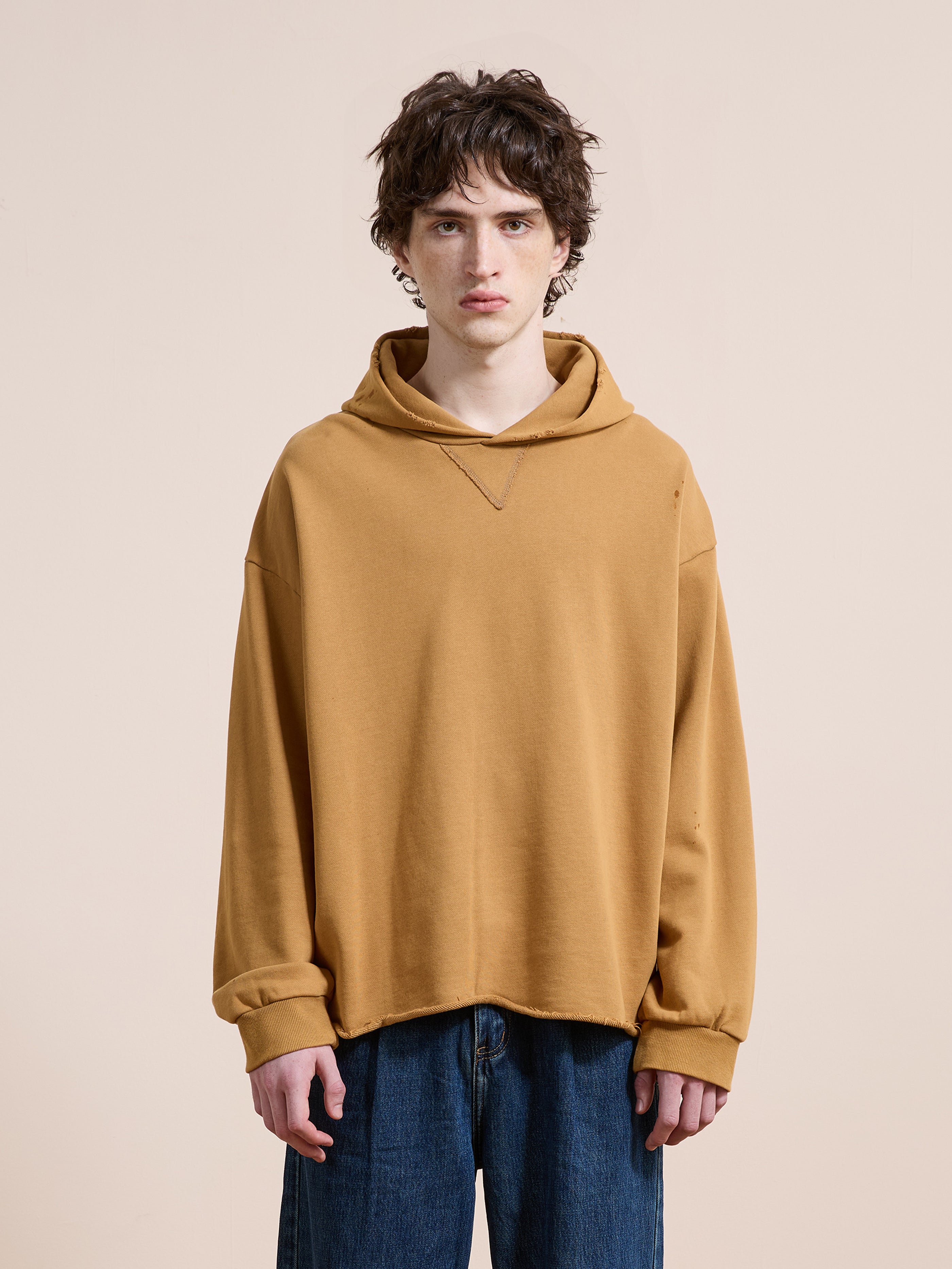 A person with short, wavy brown hair wears the FOUND Beadwork Logo Hoodie in a unisex relaxed fit with blue jeans, standing against a plain beige background.