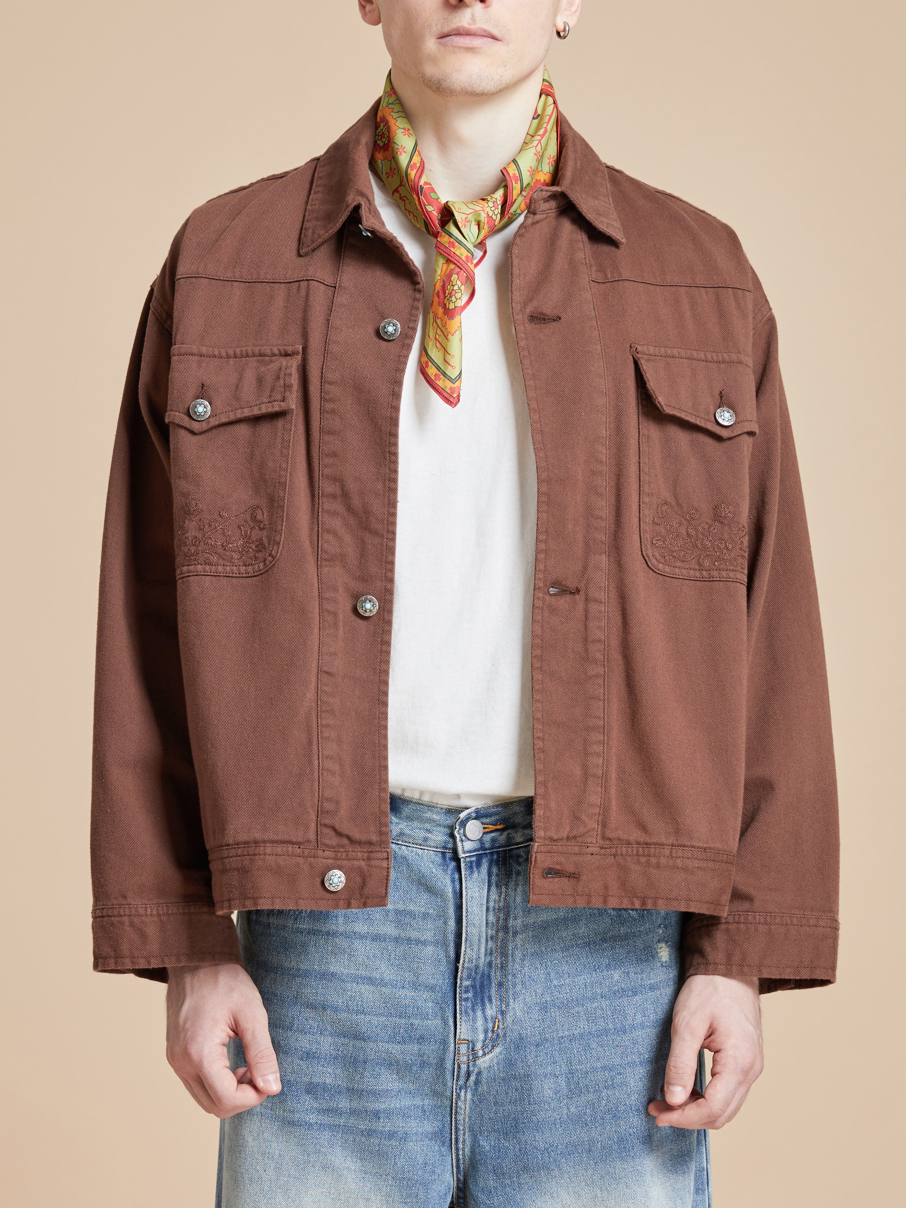 A man wearing a brown jacket and jeans with Found's Botanical Mosaic Bandana, featuring Indo-Aryan prints and made of cotton blend fabric.