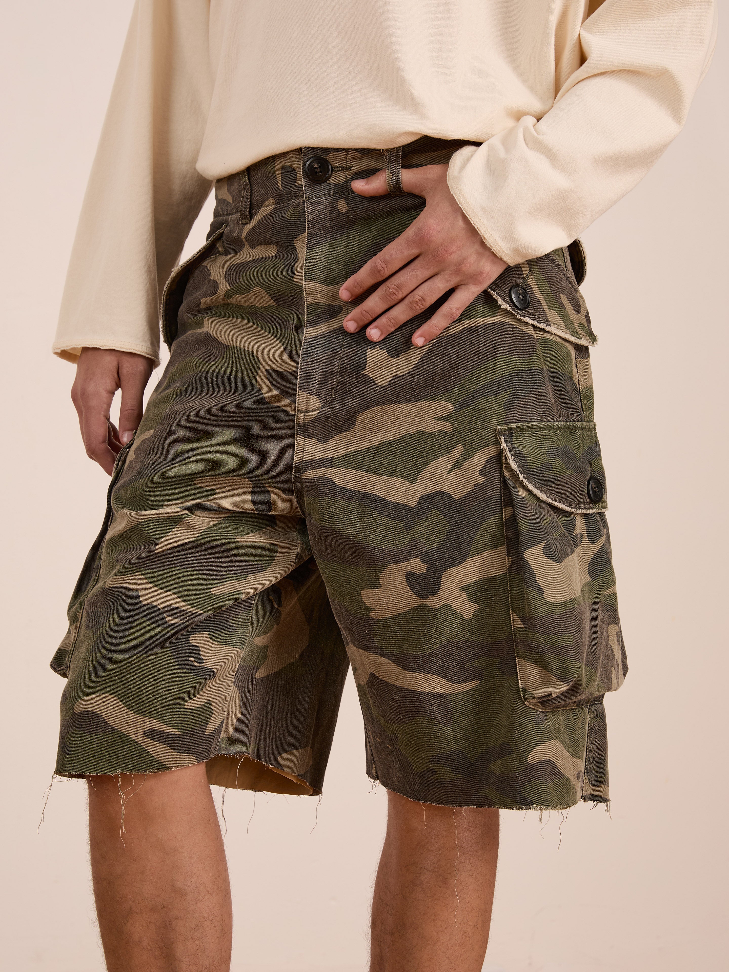 Model wears FOUND Camouflage Twill Utility Cargo Shorts and a light long-sleeve shirt, highlighting the unisex relaxed fit with one hand resting casually on the waistband.