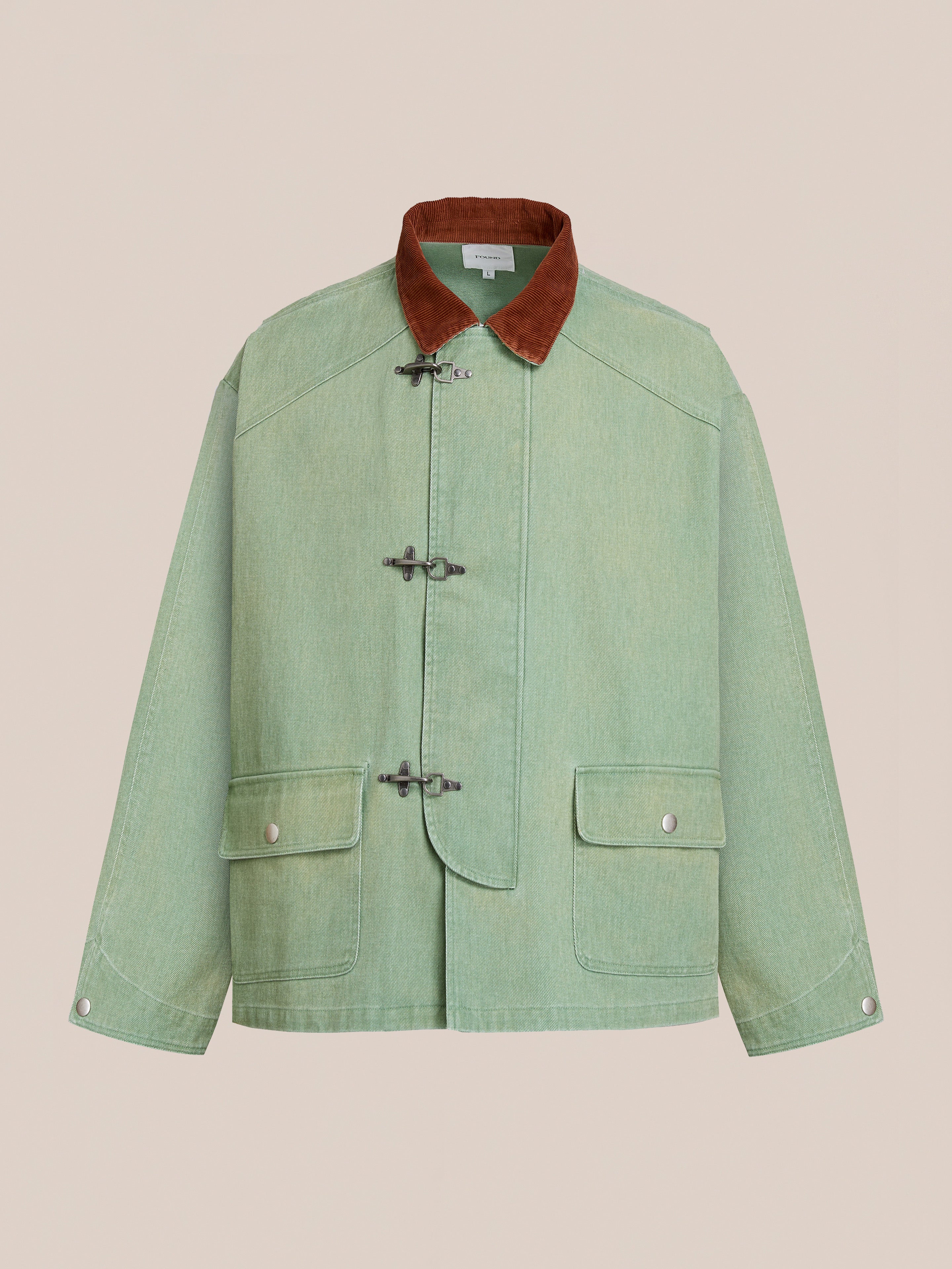 The Found Washed Fireman Clasp Workshop Jacket is a light green unisex jacket with a brown corduroy collar, toggle front closures, buttoned front flap pockets, and long sleeves, shown on a plain beige background.