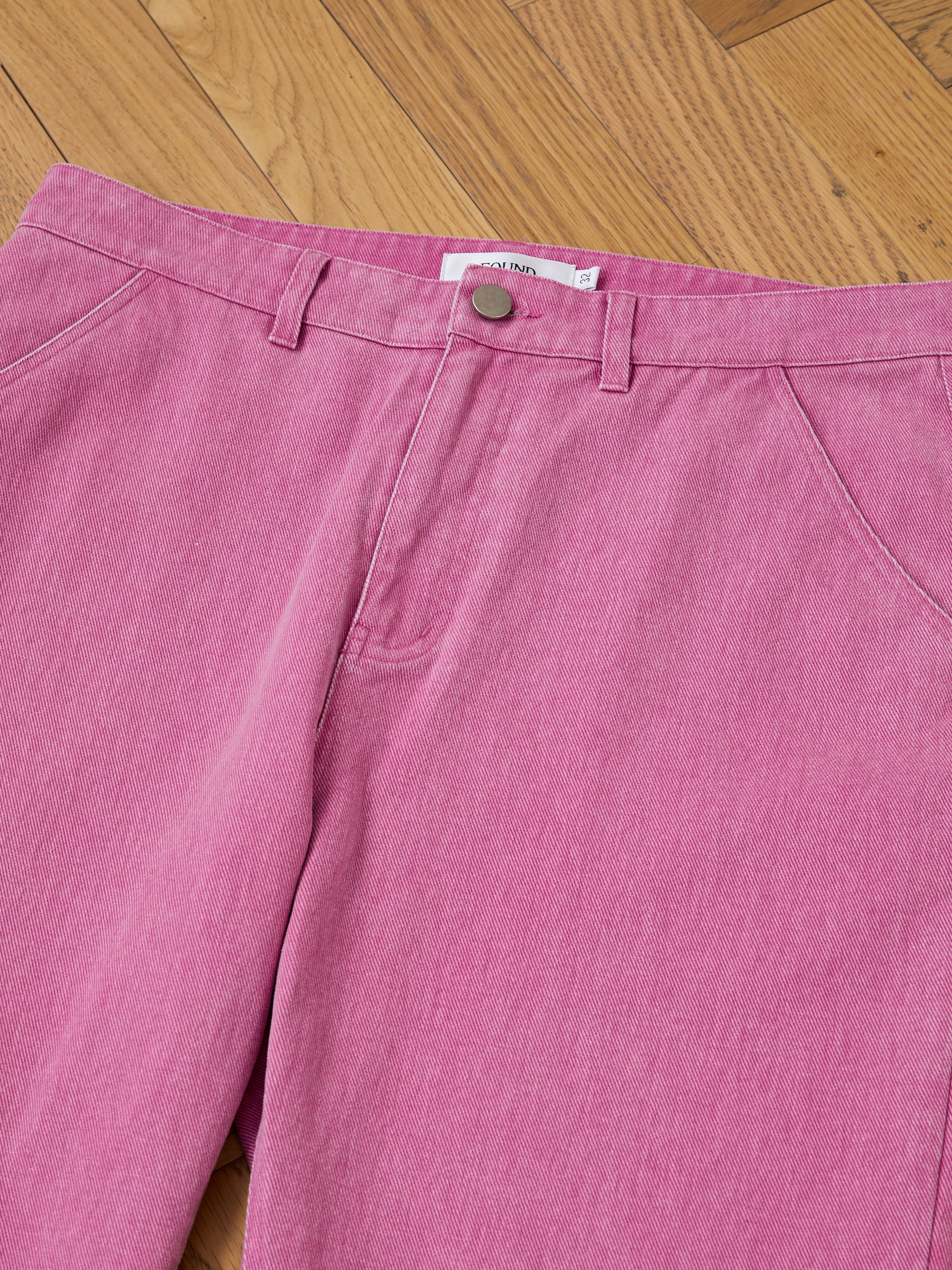 FOUND Flare Work Pants in pink, featuring a relaxed fit, belt loops, and a front button, displayed laid flat on a wooden floor.