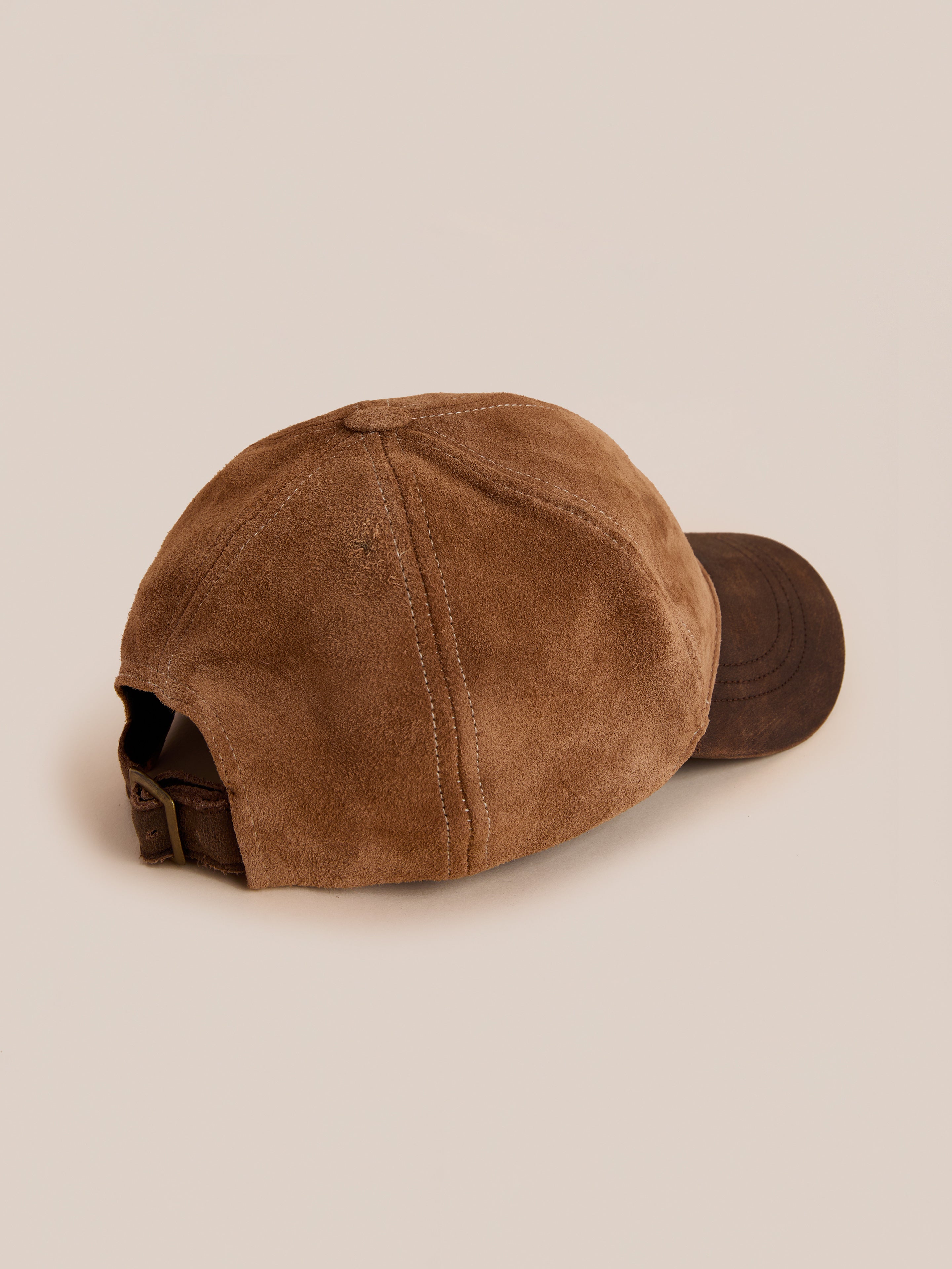 The Found Suede Leather Contrast Distressed Cap features brown suede, visible stitching, an adjustable leather strap, and a distressed leather brim, shown from the back against a neutral background.