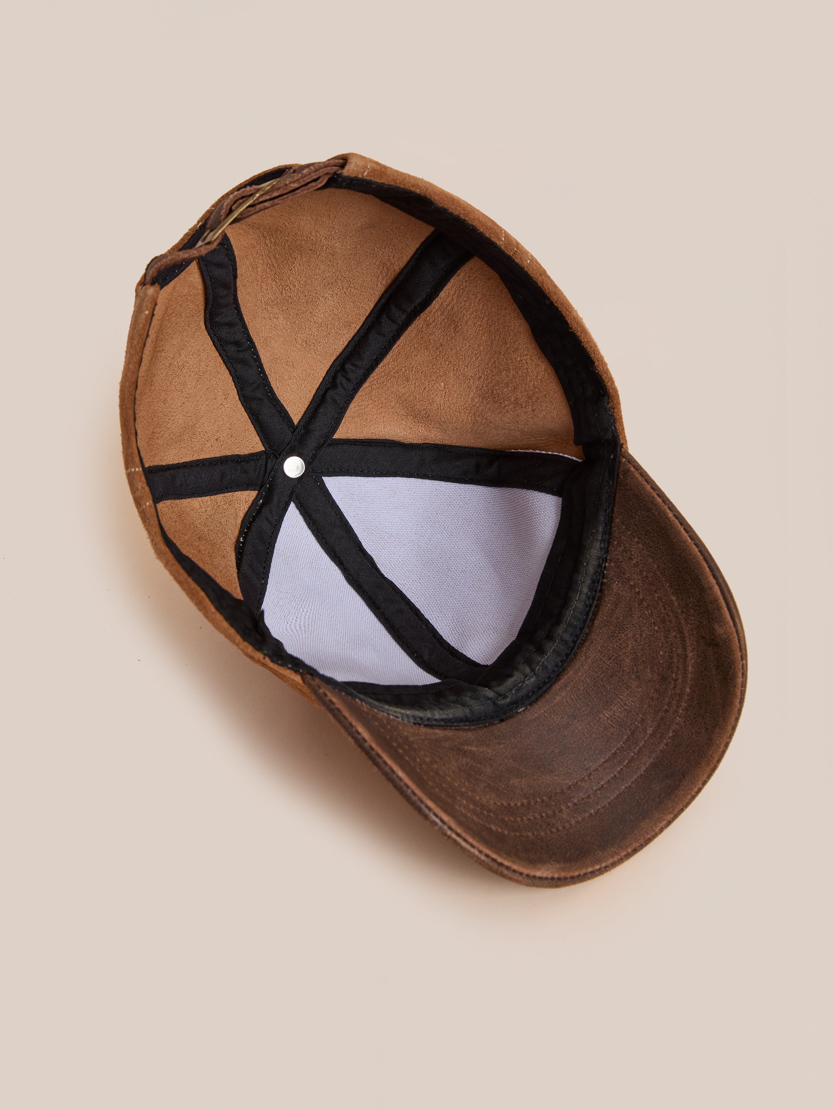 The Found Suede Leather Contrast Distressed Cap features brown suede, black inner lining, exposed stitching, and an adjustable leather strap, shown from the inside.
