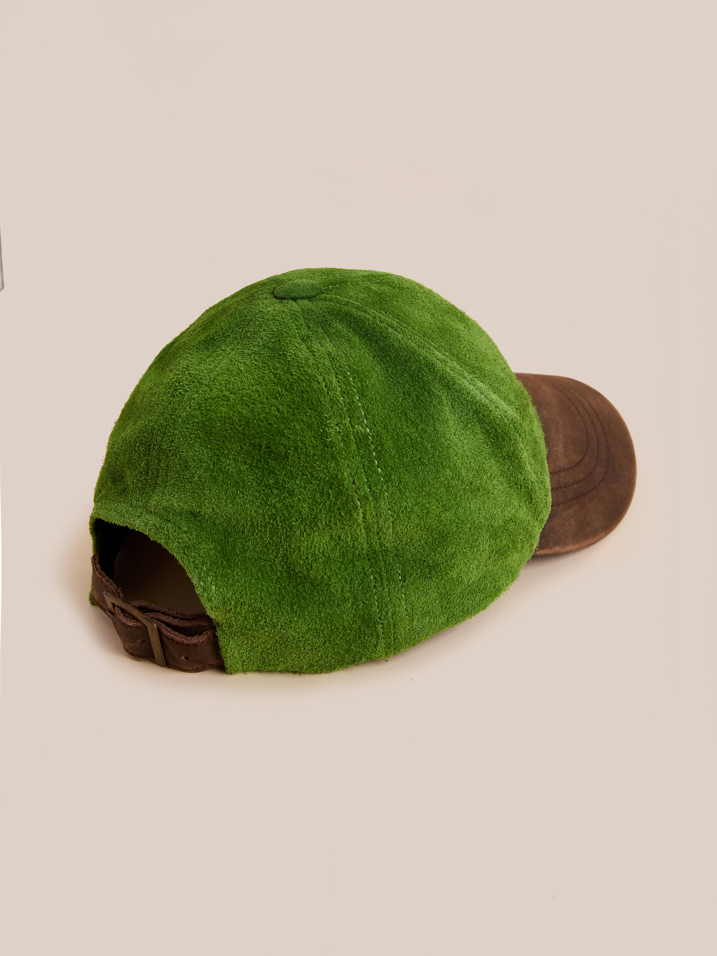 The Found Suede Leather Contrast Distressed Cap features a green suede crown, distressed leather brim, and an adjustable leather strap, shown against a neutral background.