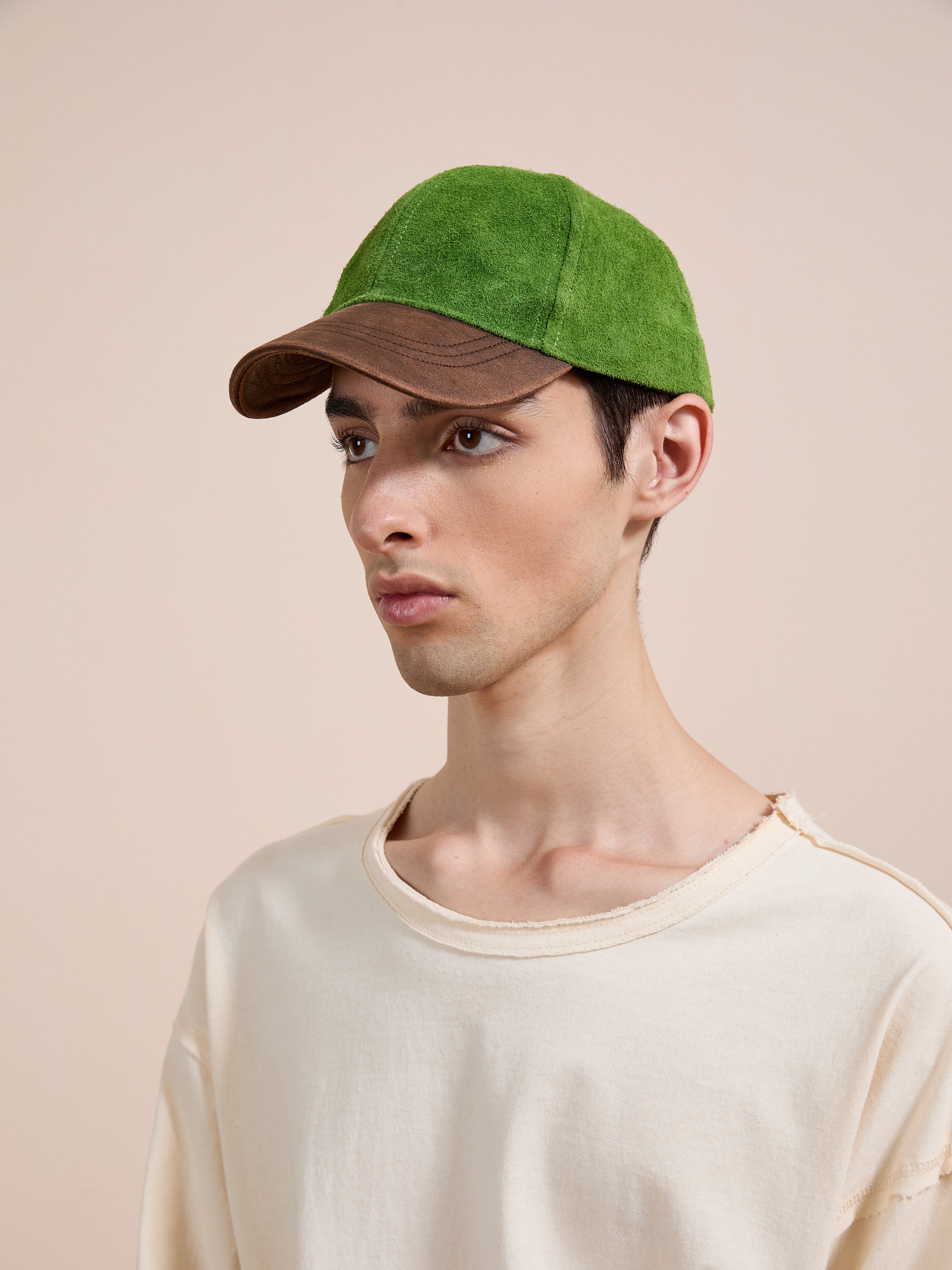 A young person in a Found Suede Leather Contrast Distressed Cap and a cream t-shirt stands against a beige background.