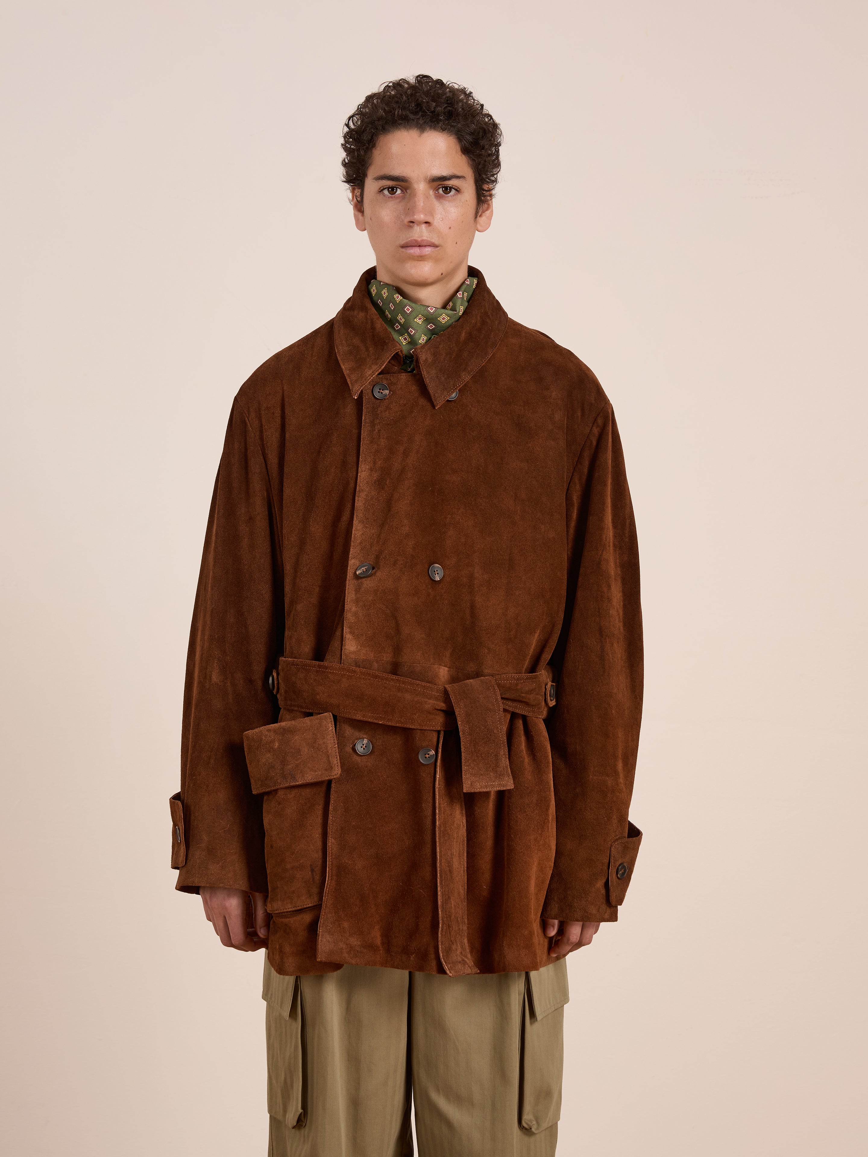 A person faces forward in a FOUND Double Breasted Suede Leather Jacket with a belt, worn over a green patterned shirt, set against a plain background.