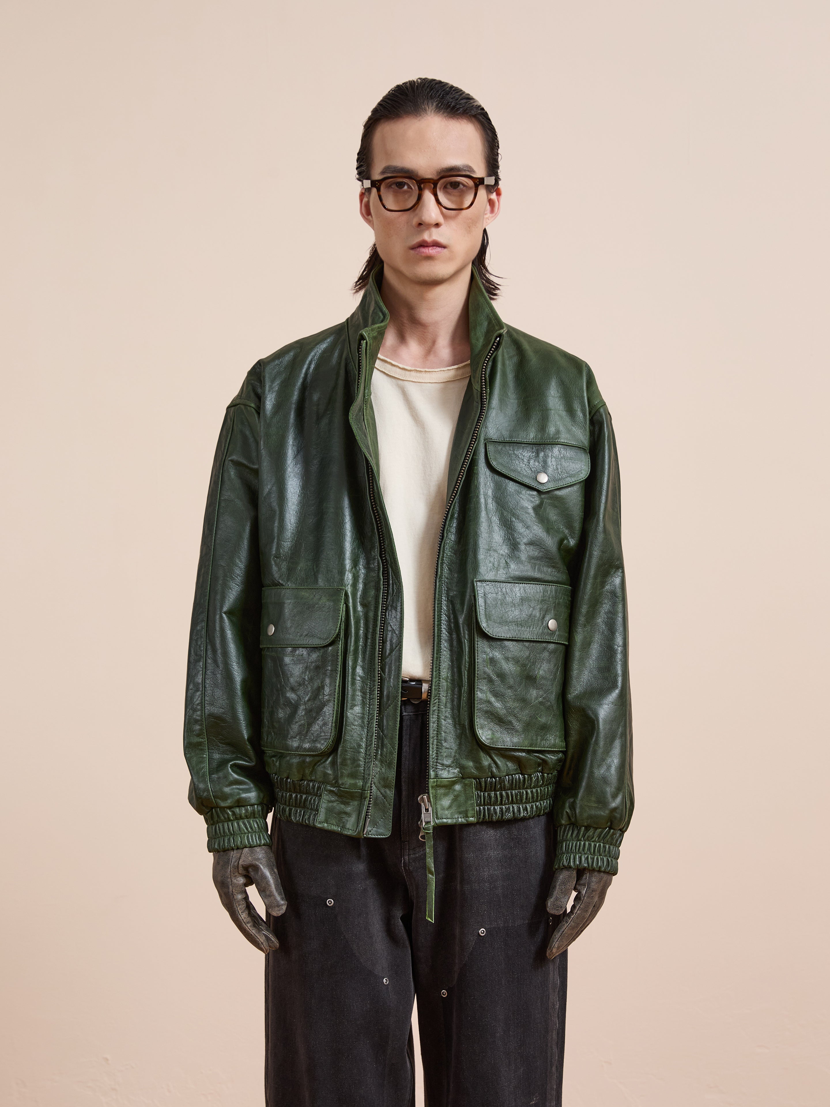 A person with long hair and glasses wears the FOUND Forest Leather Bomber Jacket over a white shirt and dark pants, standing against a neutral background.