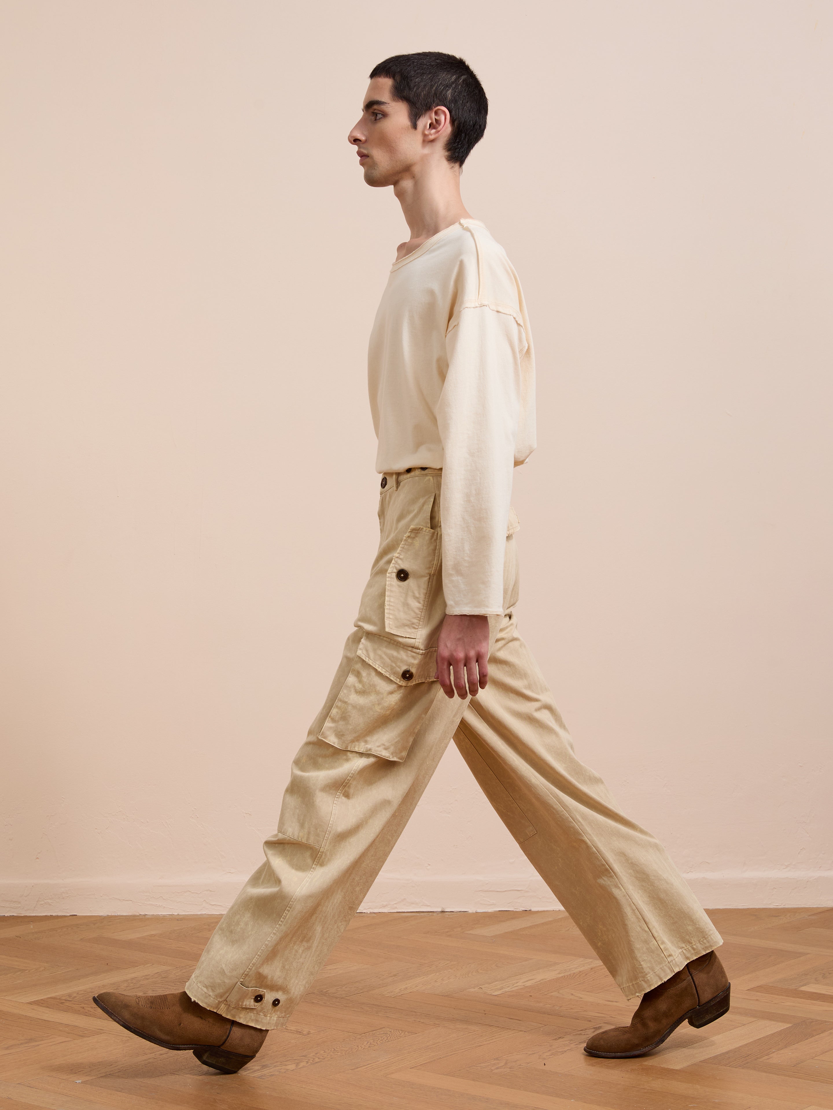 A person wearing FOUND Utility Herringbone Paneled Pants and brown shoes walks indoors on a wooden floor against a plain light-colored wall.