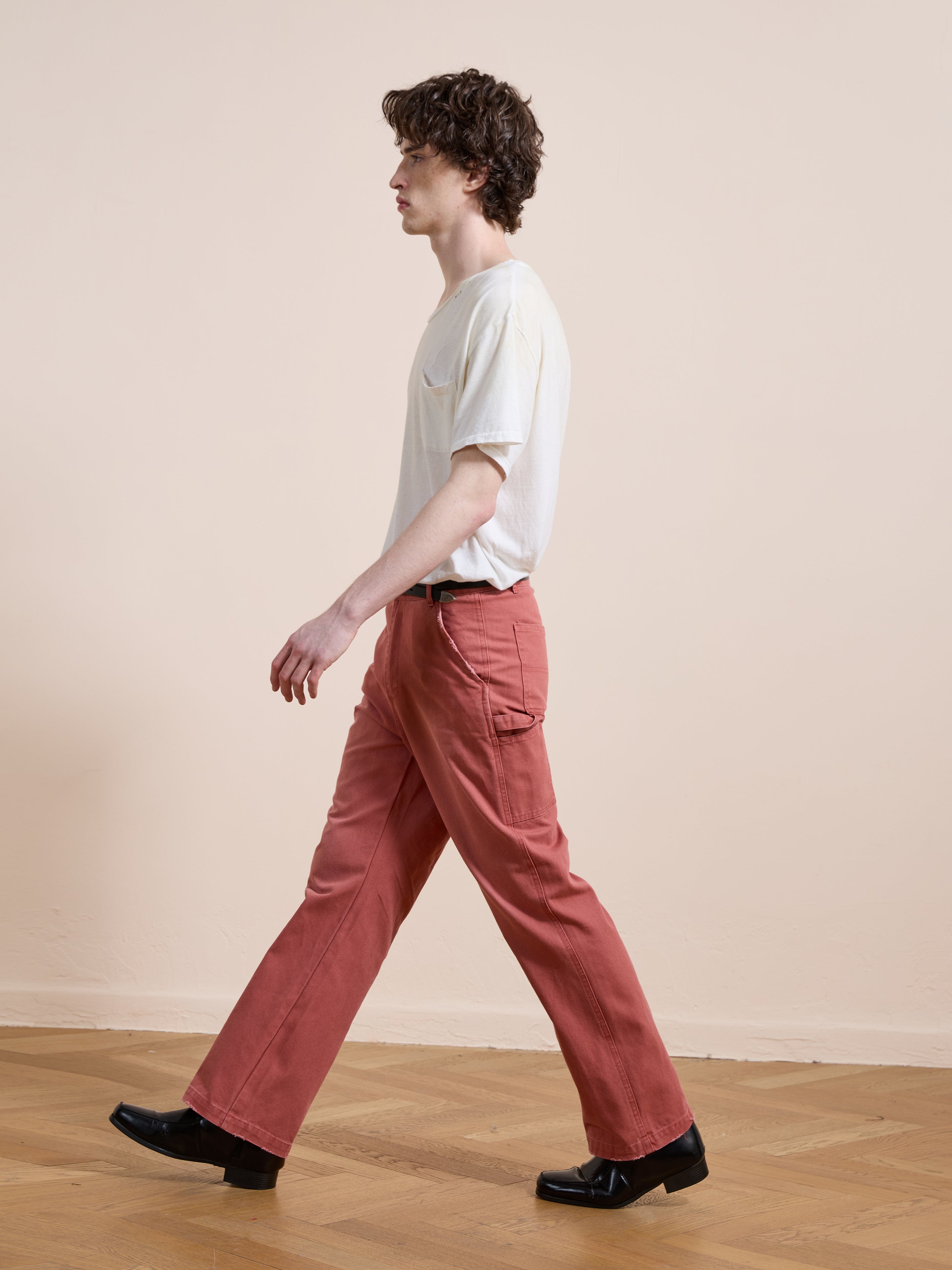 A person wears FOUND Canvas Faded Pants and a white t-shirt while walking indoors on a wooden floor against a plain light-colored wall.
