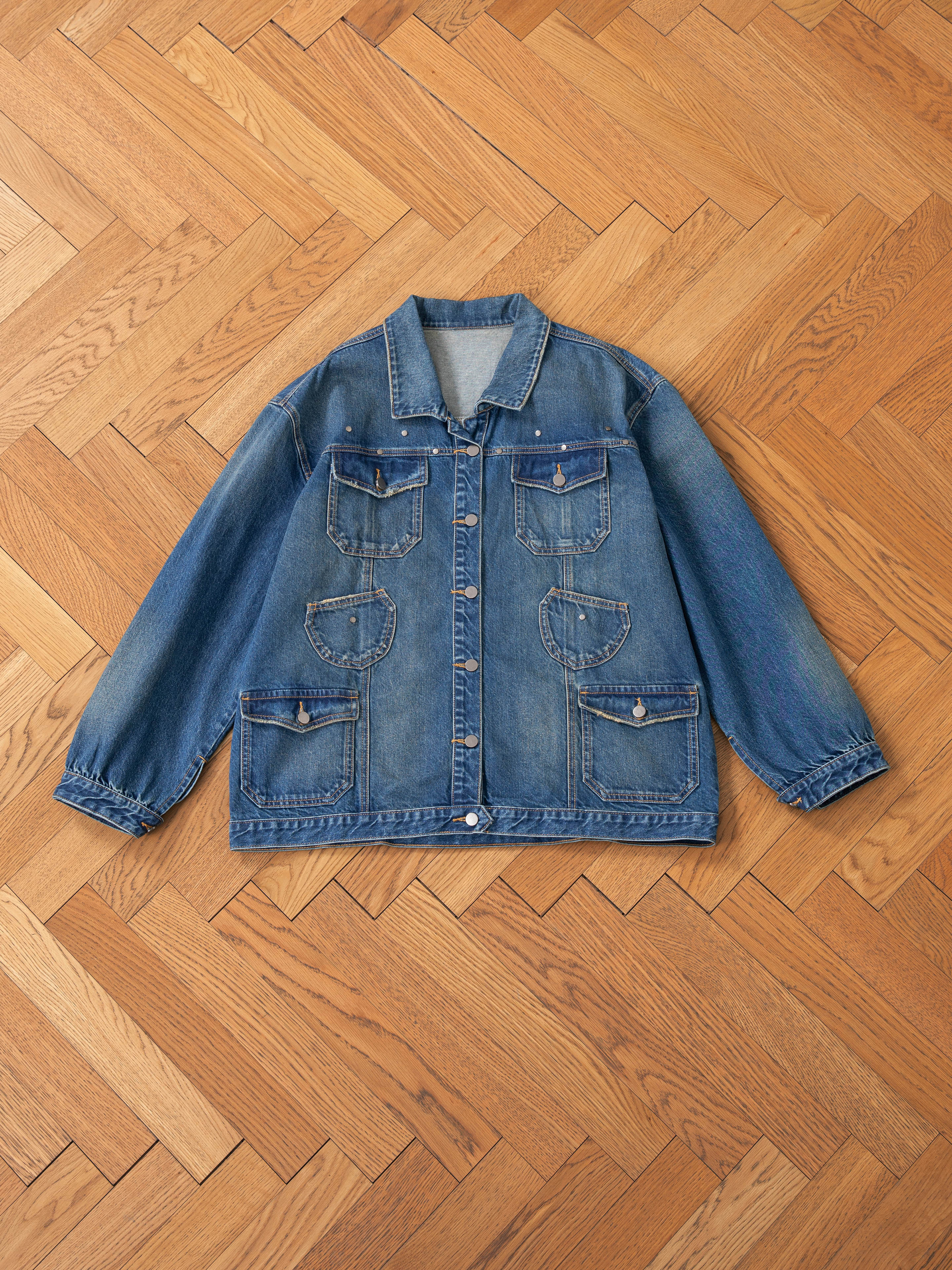 FOUND's unisex Denim Carpenter Jacket, featuring a relaxed fit and four front pockets, resting on a wooden herringbone-patterned floor.
