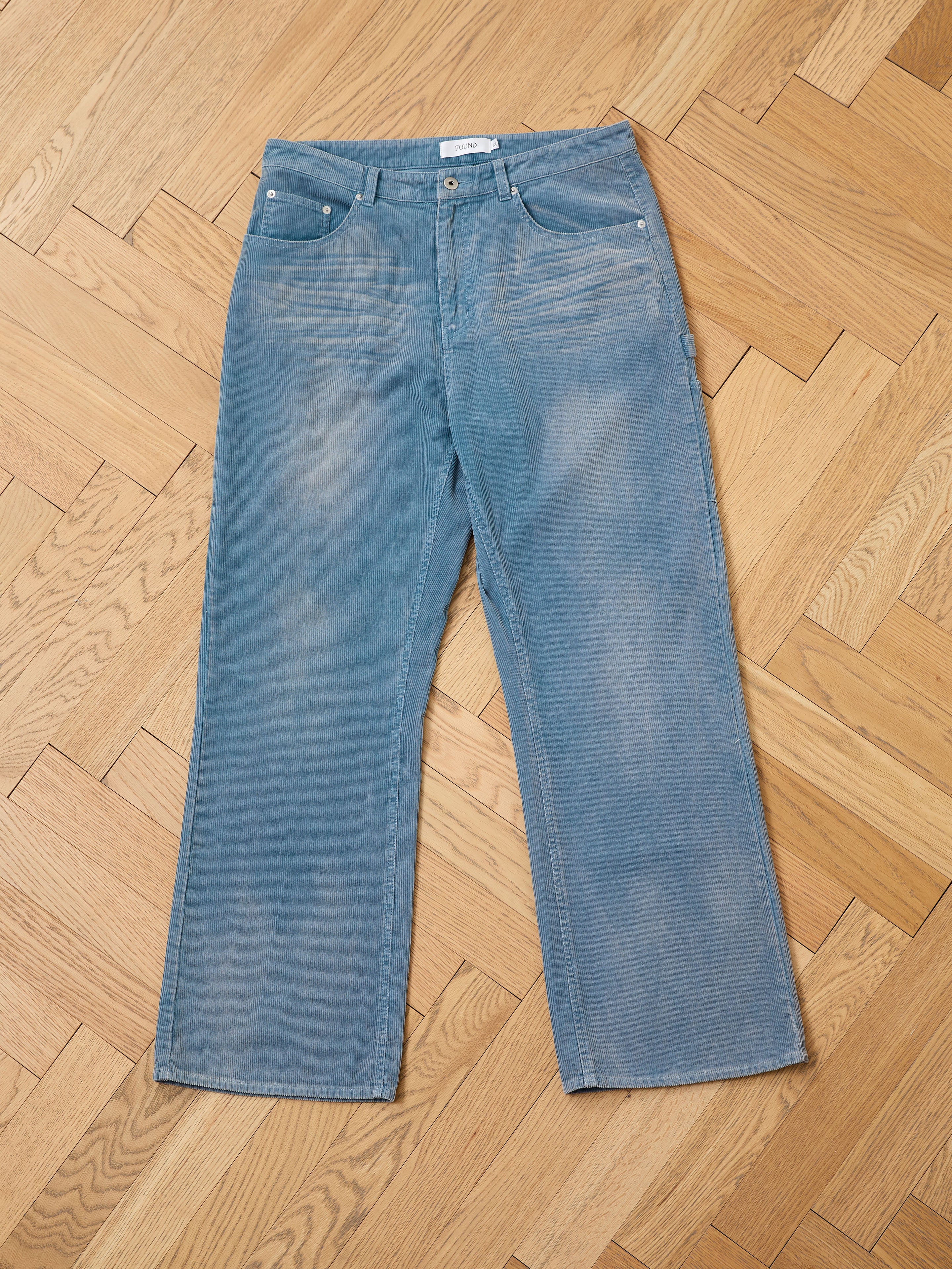 FOUND Corduroy Flare Work Pants in light blue, featuring a relaxed vintage-inspired fit, displayed flat on a wooden parquet floor.