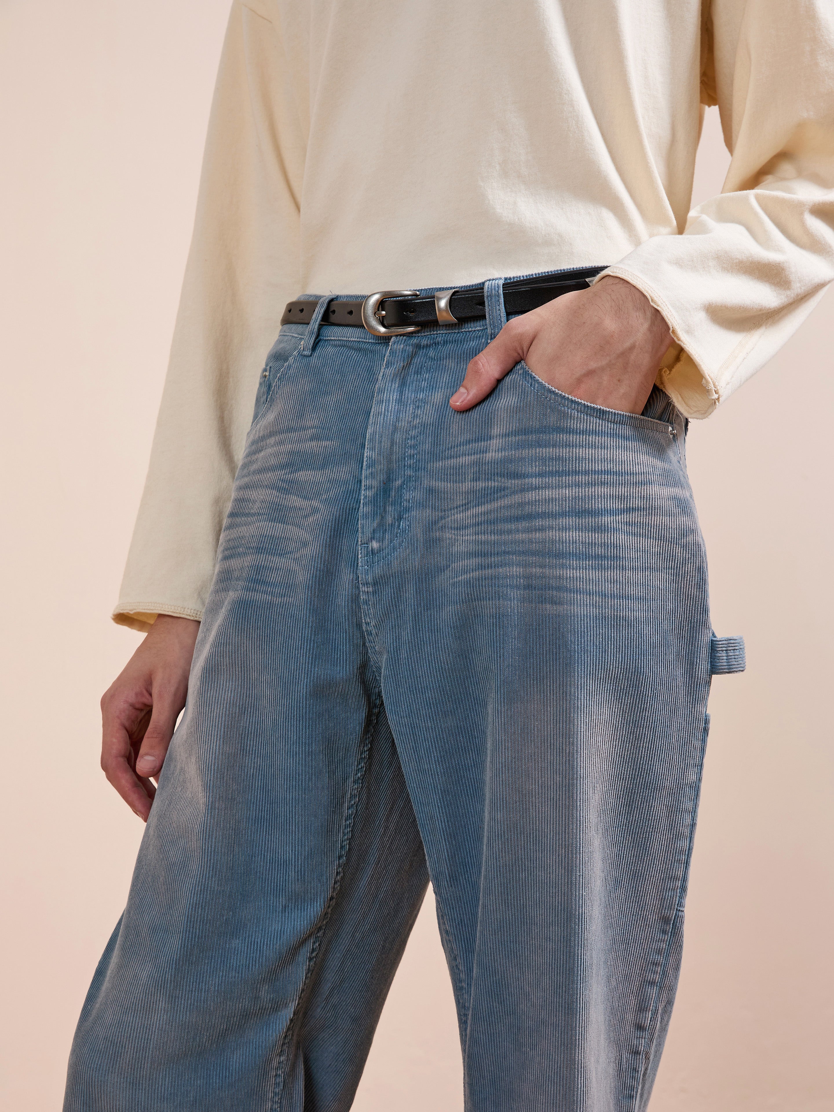 Model wearing FOUND Corduroy Flare Work Pants in vintage blue with a relaxed fit, styled with a cream long-sleeve shirt, black belt, and one hand in their pocket, shown from shoulders to thighs.