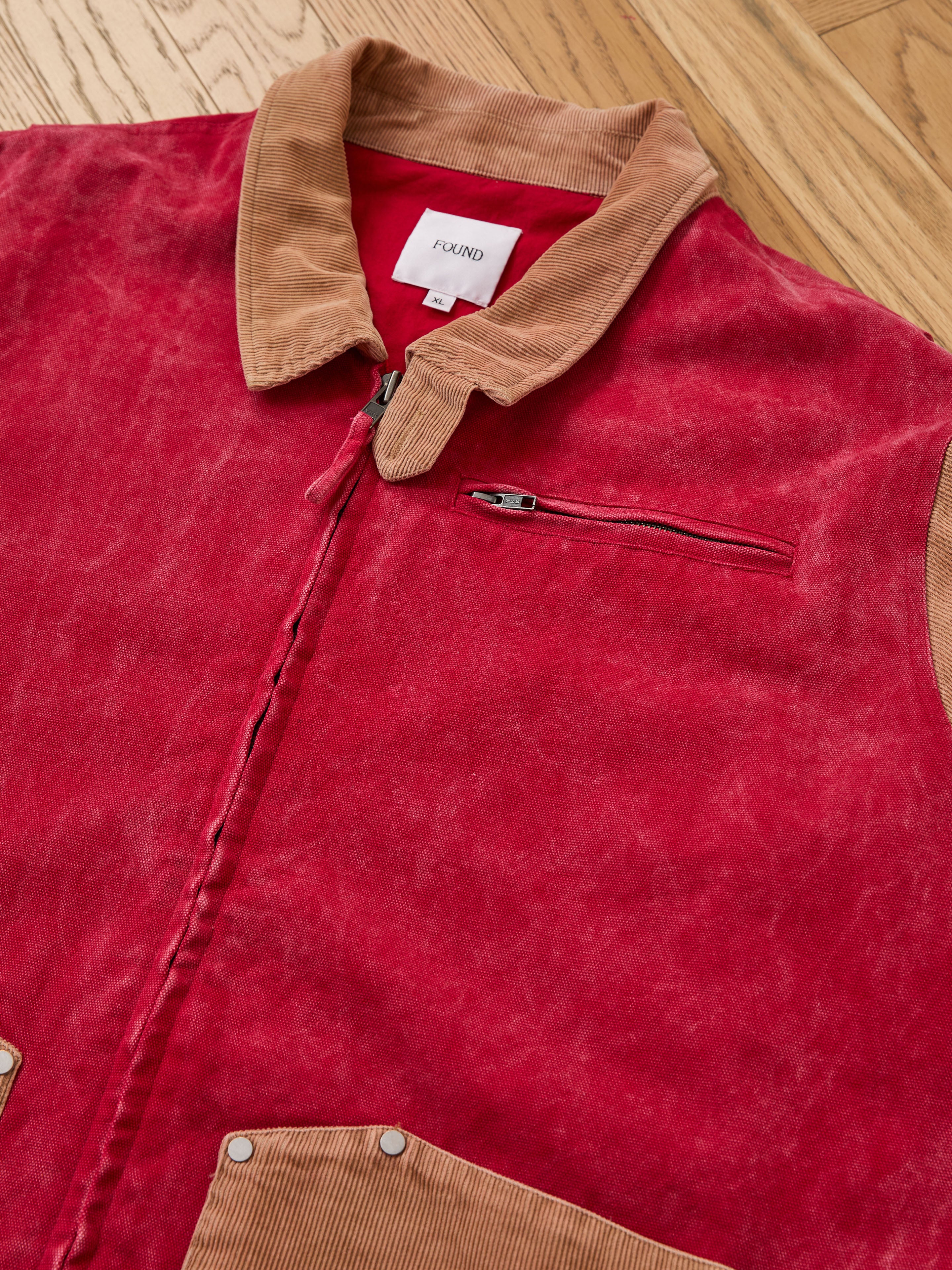 The Found Corduroy Field Jacket—red with a tan collar and pocket flaps, zippered chest pocket, and visible “FOUND” label—offers a unisex relaxed fit for versatile style.