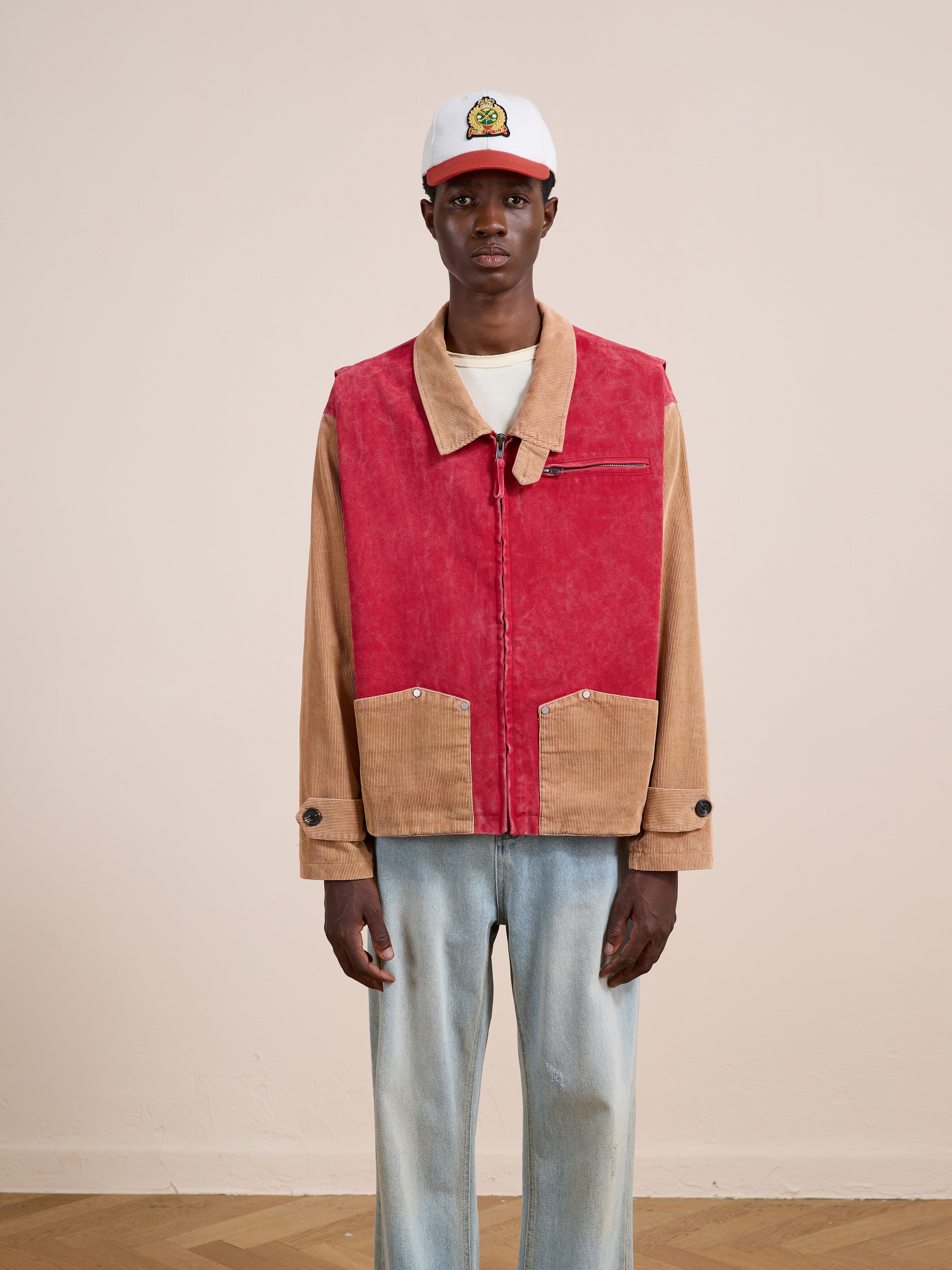 A person in Found's Corduroy Field Jacket, styled with light blue jeans, a white t-shirt, and a white cap, stands against a plain beige background.