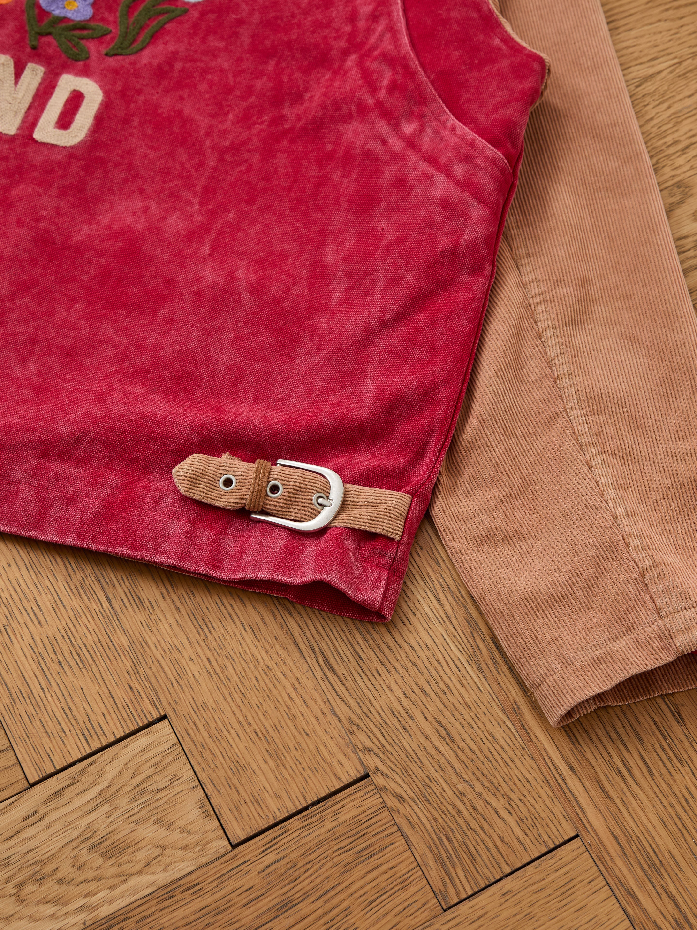 Close-up of the Found Corduroy Field Jacket: features a red body, brown corduroy sleeve, and decorative brown strap with a silver buckle—ideal for any unisex workwear fan.