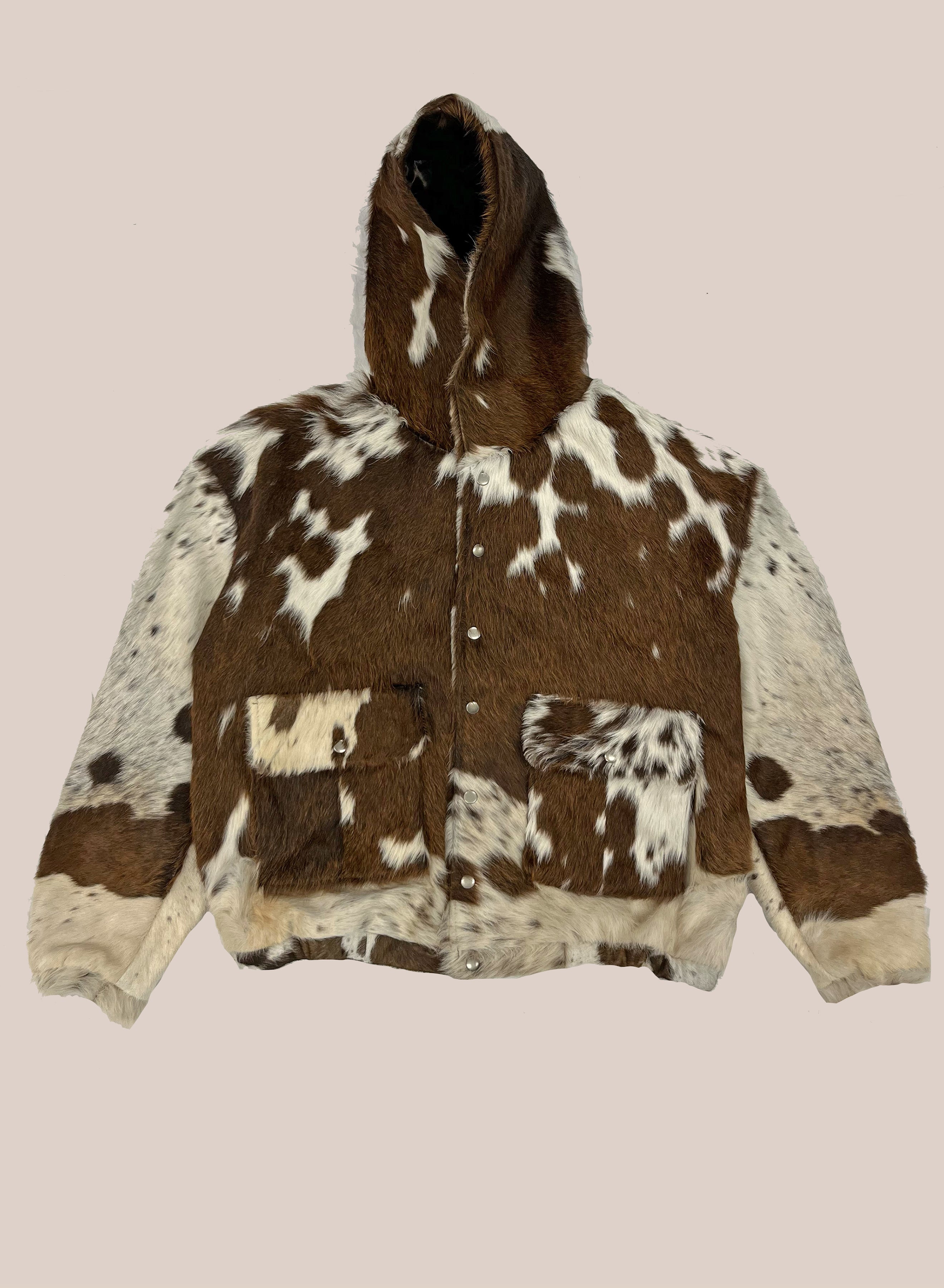 The FOUND Cowhide Drover Hoodie features a brown and white cowhide pattern, front buttons, two large pockets, and a relaxed unisex fit—perfect for versatile everyday wear.
