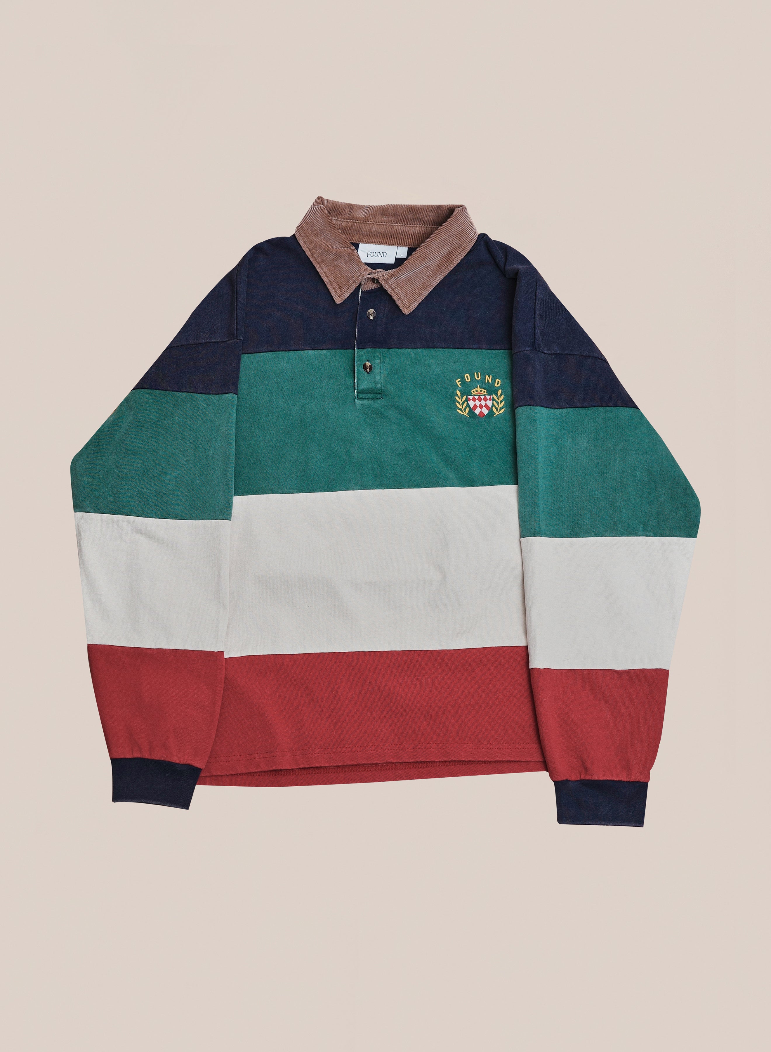 The FOUND Crestfield Rugby is a unisex relaxed fit shirt with navy, green, white, and red stripes, a brown collar, and an embroidered crest on the left chest, shown laid flat on a beige background.