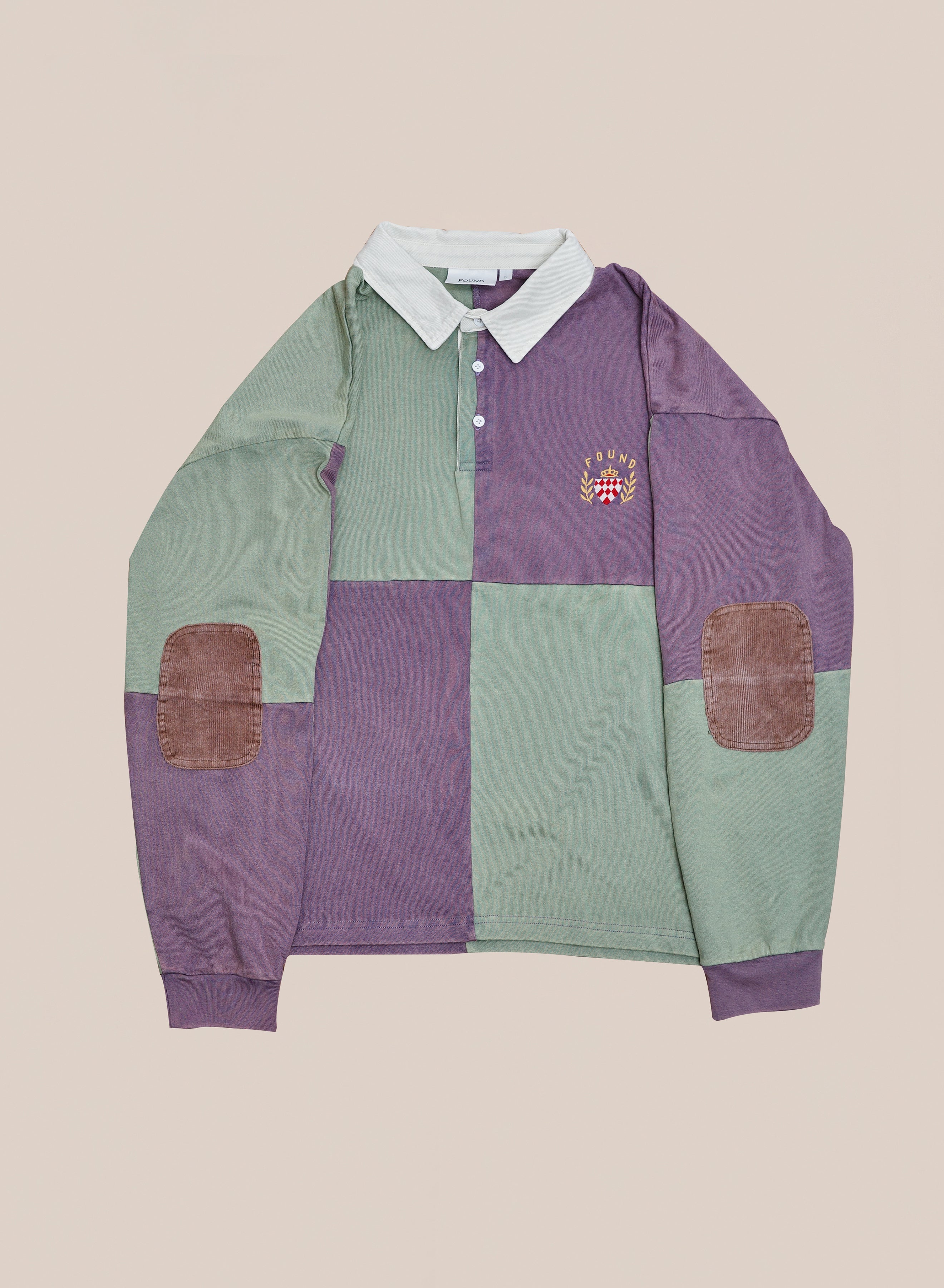 FOUND Crestfield Rugby shirt with green and purple color blocks, brown corduroy elbow patches, white collar, and embroidered crest. Unisex athletic top, shown laid flat on a beige background.
