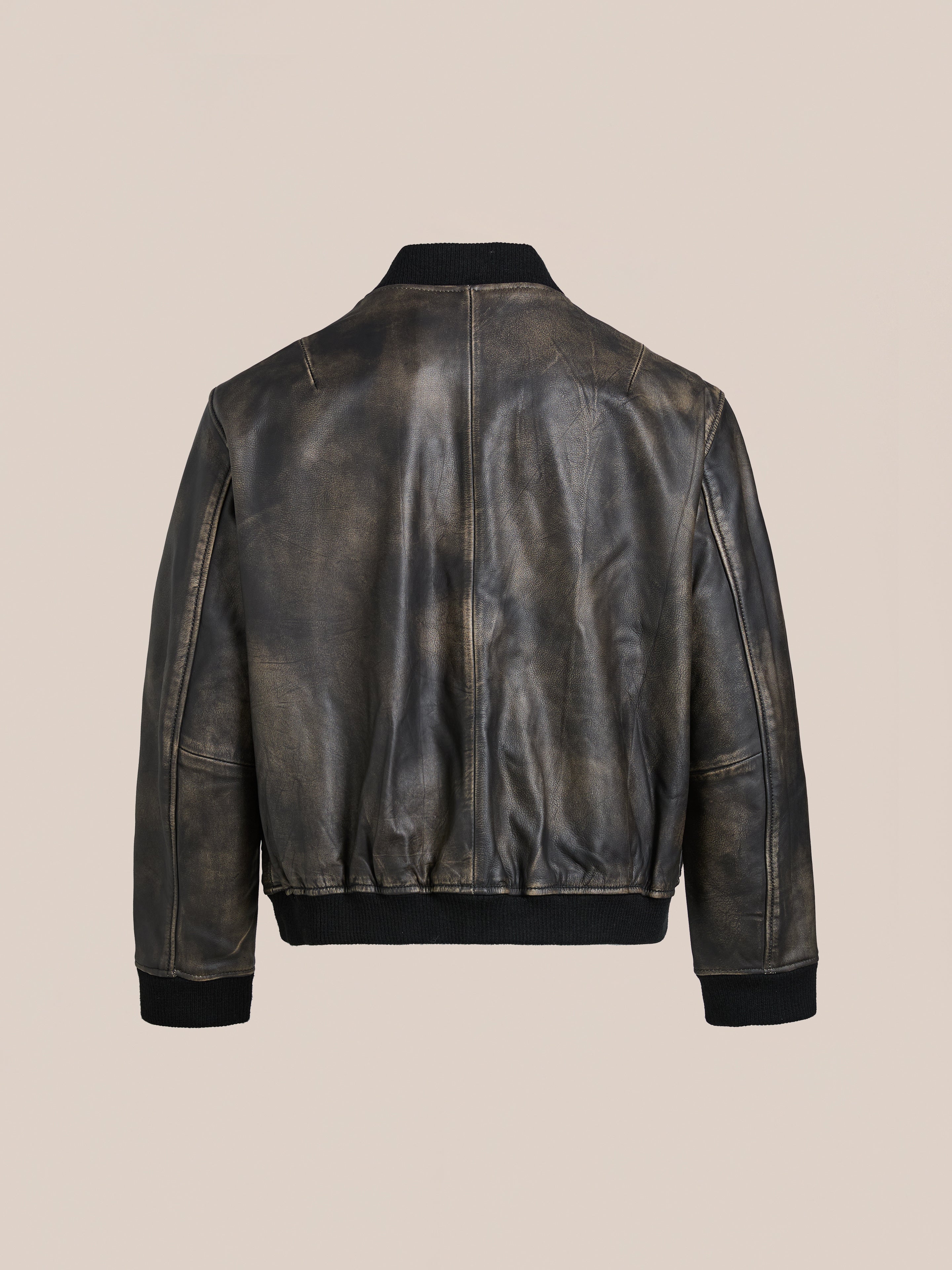 Back view of Found's Distressed Pavement Leather Bomber Jacket, a vintage-inspired piece made from genuine cowhide, with black ribbed cuffs and waistband against a beige background.