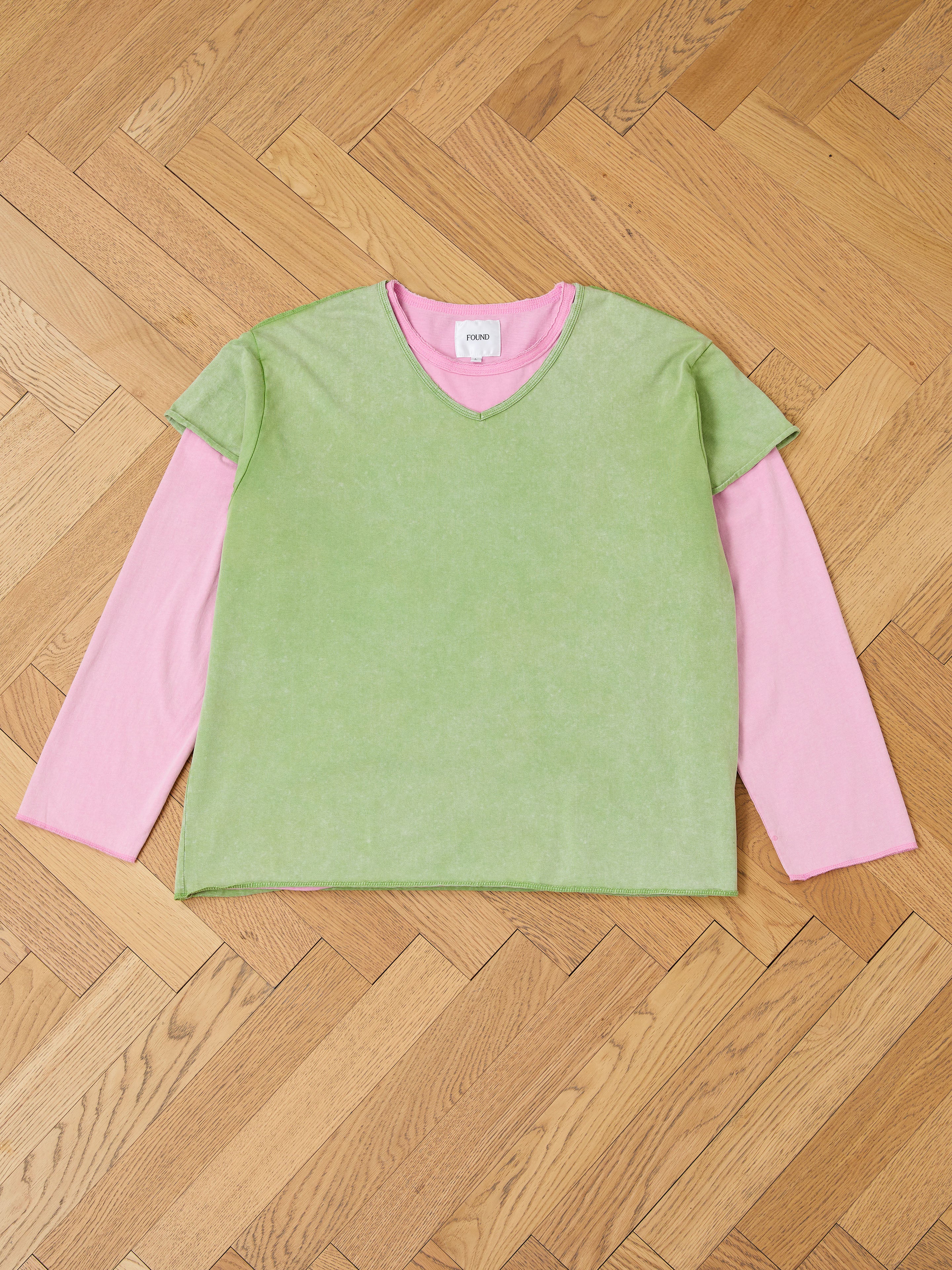 The FOUND Double Layer LS Tee, featuring a sunfade wash green short-sleeve V-neck over a pink unisex long sleeve, is displayed flat on a wooden herringbone floor.