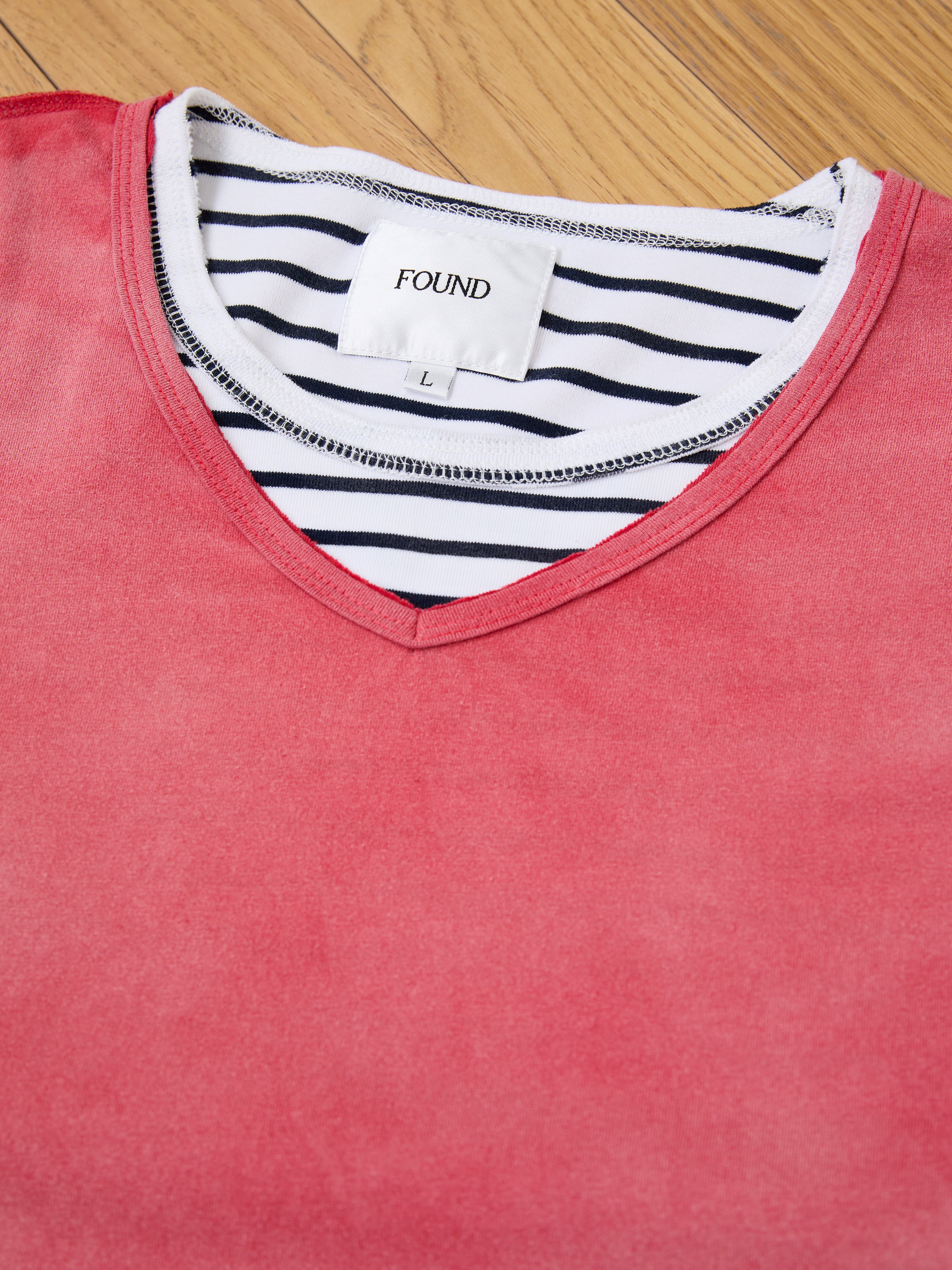 A red V-neck top is layered over a black and white striped FOUND Double Layer LS Tee, with both garments lying on a wooden surface.