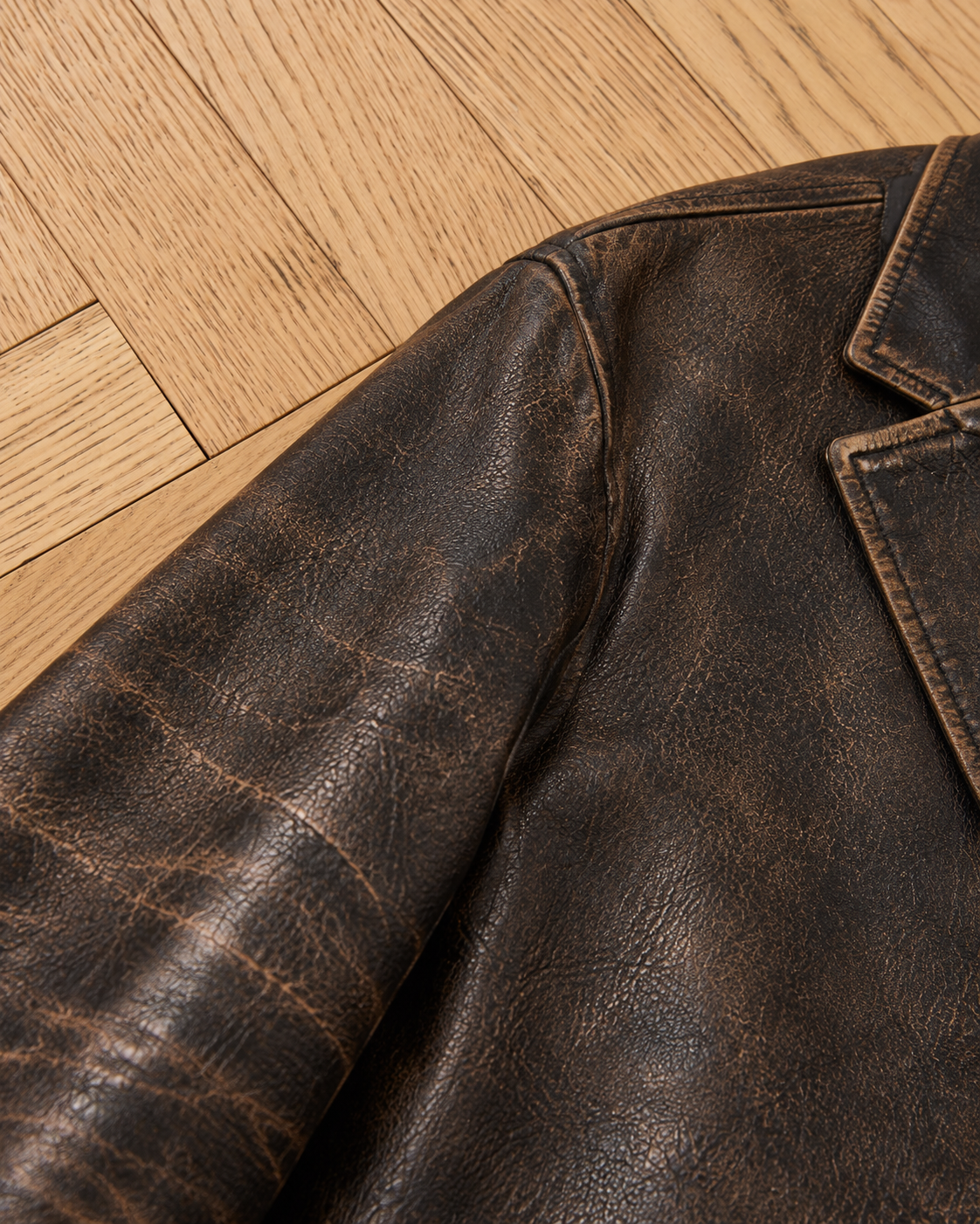 Close-up of the shoulder and sleeve of the FOUND Distressed Leather Blazer on light wood flooring, highlighting its rich genuine leather texture.