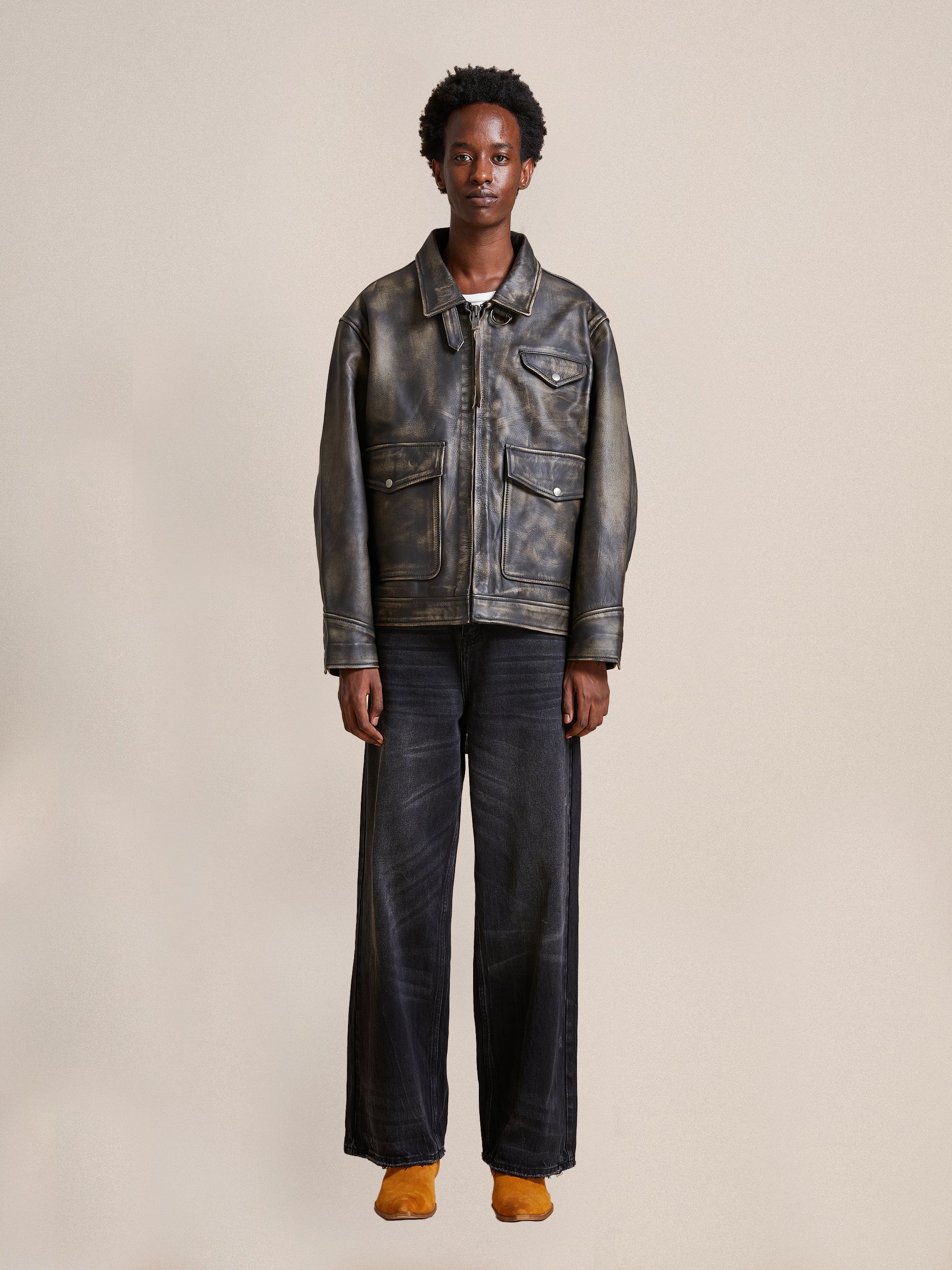 A person stands facing forward, wearing the Found Distressed Leather Pocket Jacket, wide-leg jeans, and orange socks against a plain background.