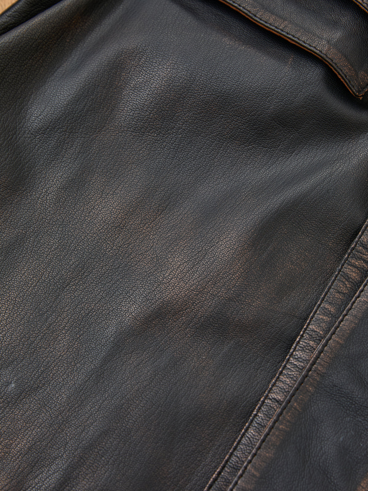 Close-up of the FOUND Distressed Leather Trench Coat, highlighting its worn black hand-distressed leather, visible creases, and detailed stitching along the edge.