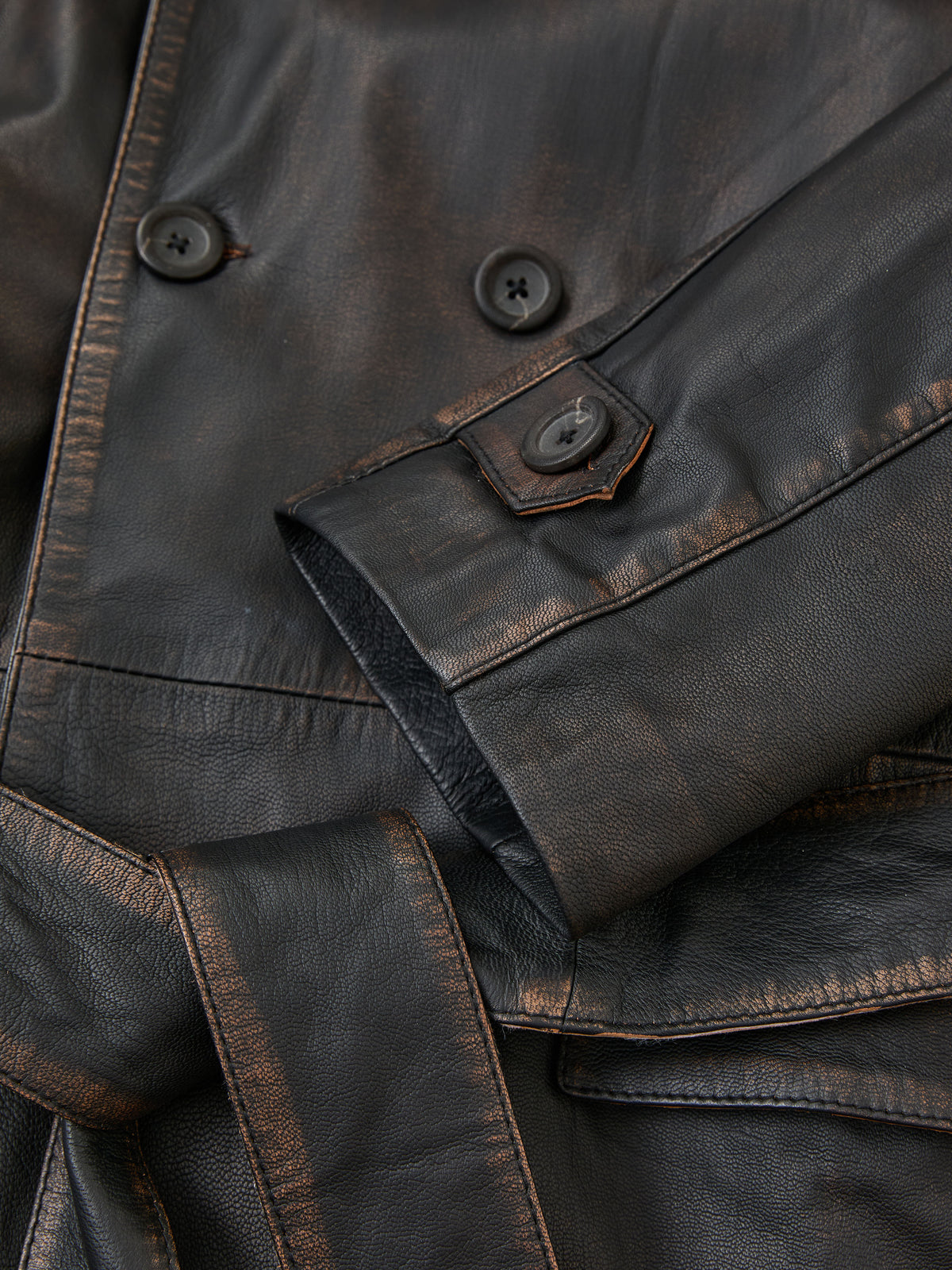 Close-up of a FOUND Belted Leather Trench Coat, highlighting brown worn leather, buttons, a sleeve, and part of the belt.