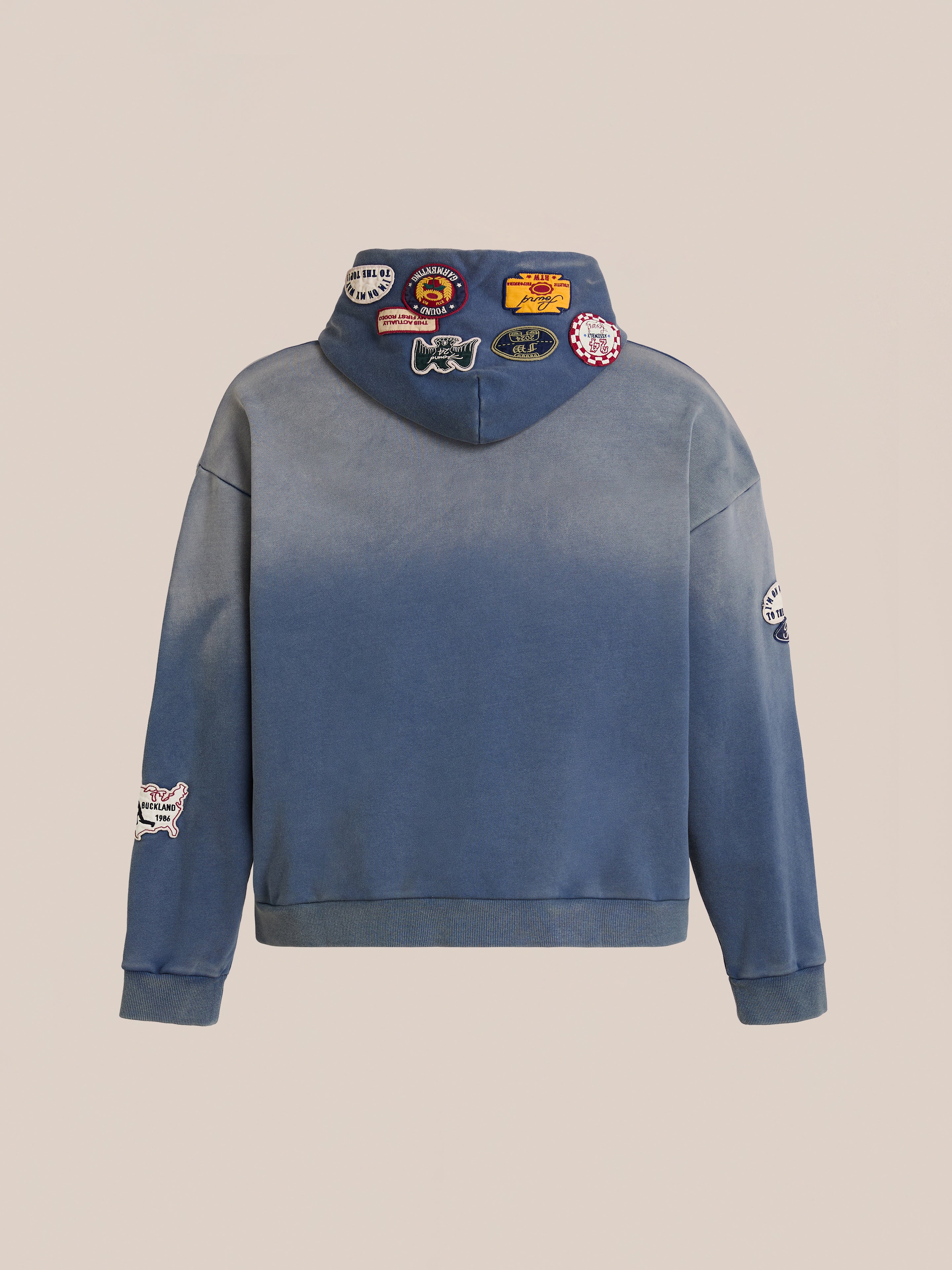 The FOUND Distressed Patch Hoodie is a blue vintage-style hoodie, shown from the back, with colorful patches on the hood and sleeves. Made from soft French Terry cotton, it's displayed against a neutral background.