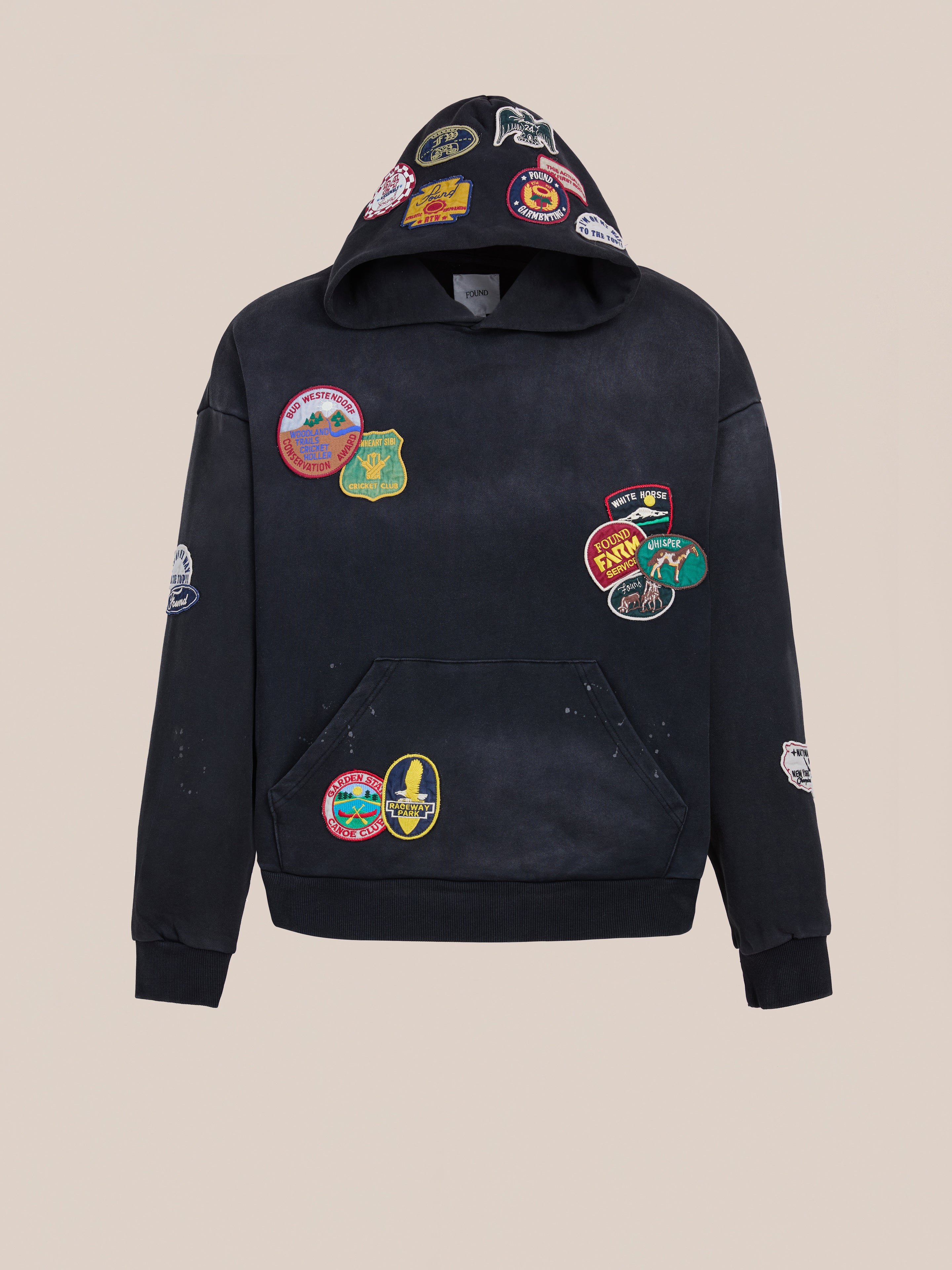 The FOUND Distressed Patch Hoodie in vintage washed black showcases multiple colorful embroidered patches on the front, hood, sleeves, and pocket, set against a plain light background.
