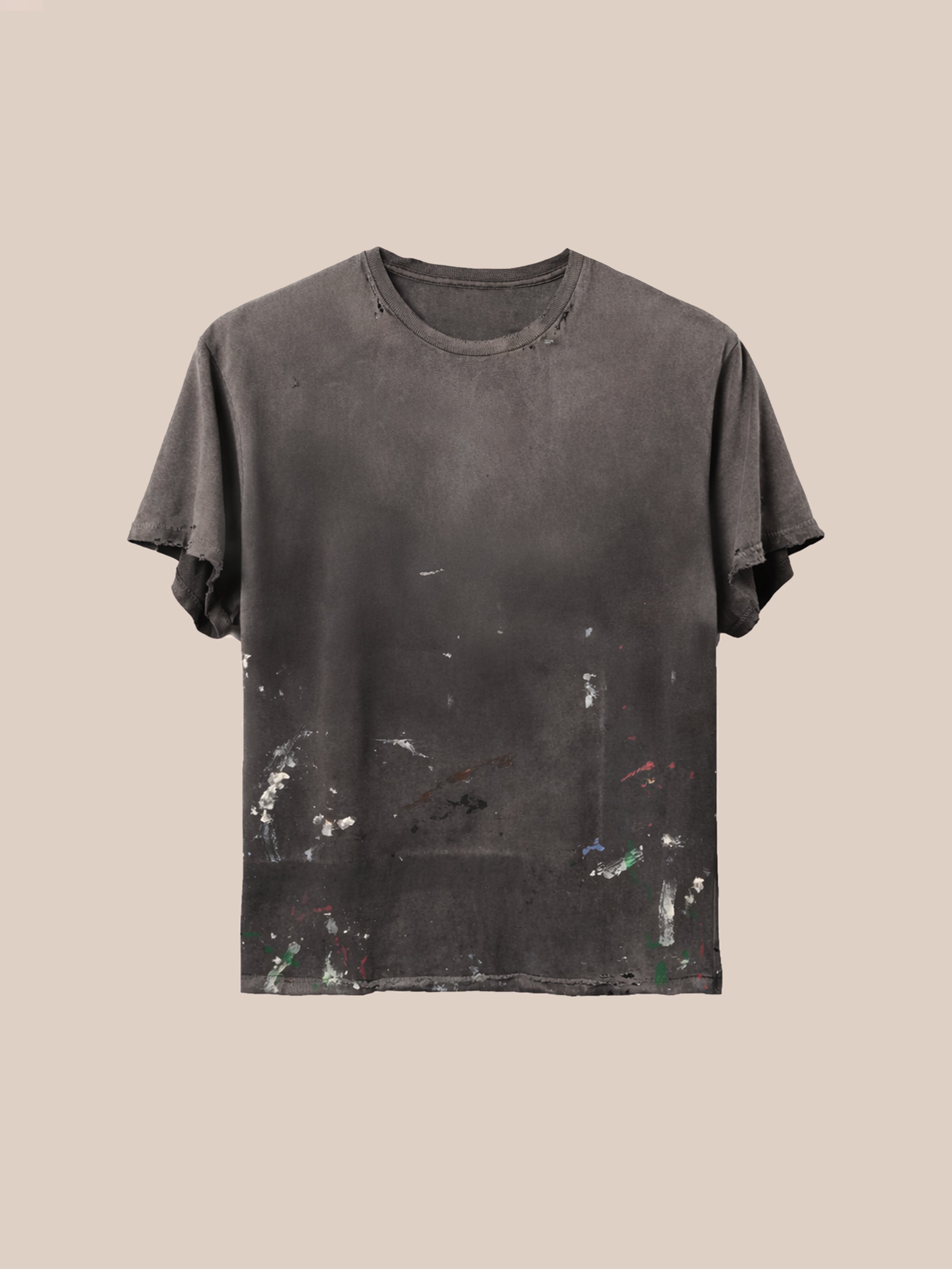 The FOUND Distressed Paint Tee, a unisex relaxed fit shirt in dark gray with faded paint stains and subtle distressing, is displayed against a neutral beige background.