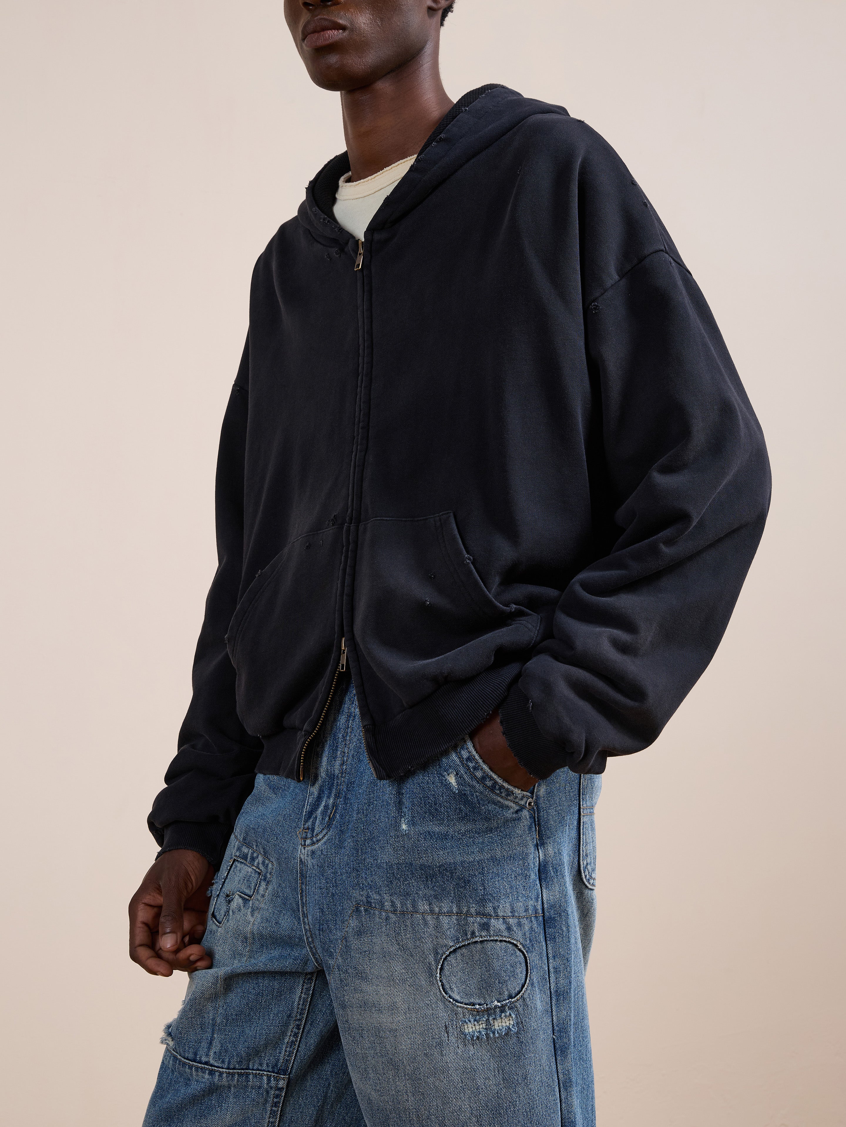 A person wearing the FOUND Distressed Thermal Lined Zip Up Hoodie in black over a white t-shirt and blue distressed jeans, standing with one hand in their pocket.