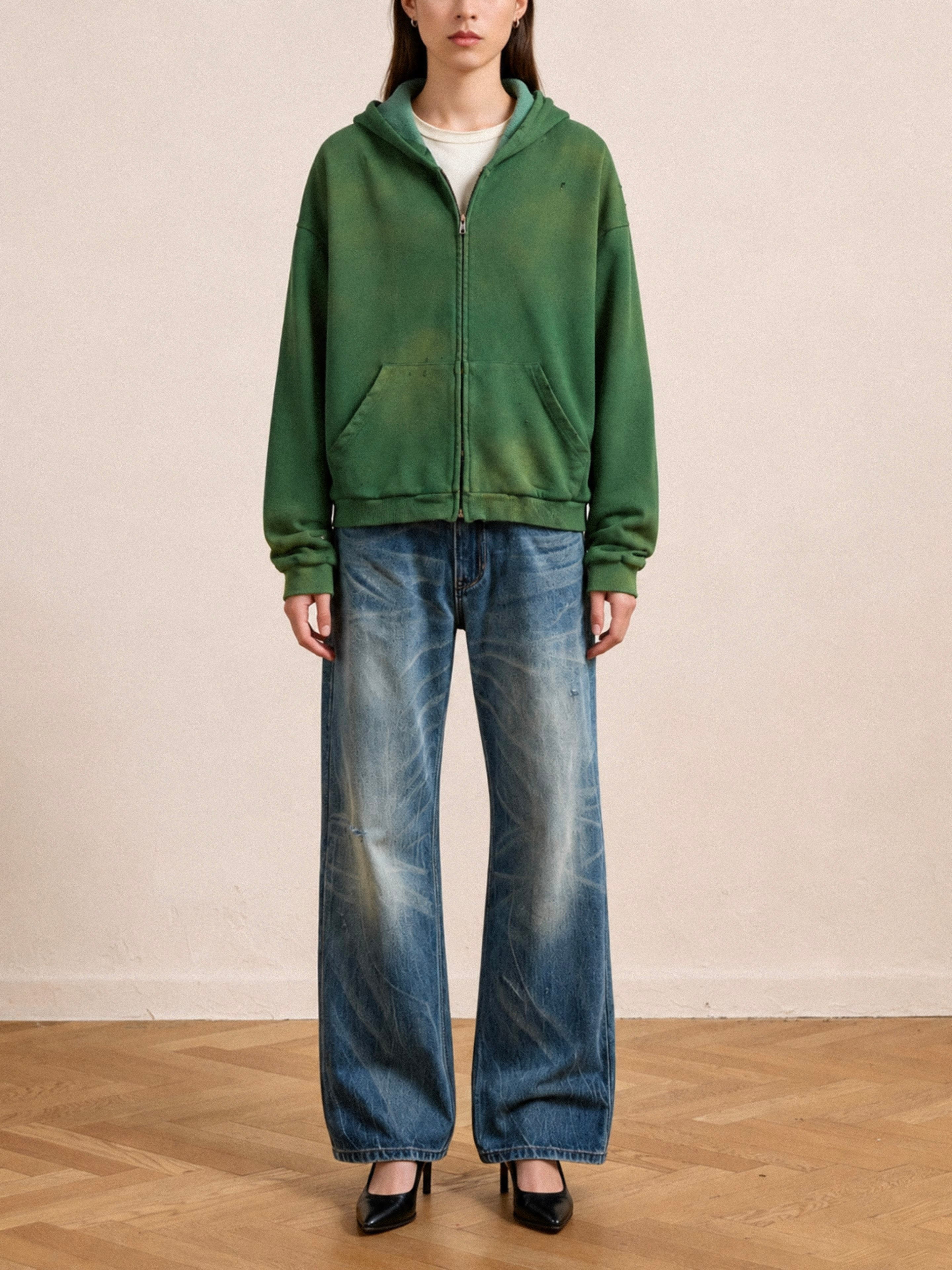 Indoors on a wooden floor, someone wears the FOUND Distressed Thermal Lined Zip Up Hoodie in green, paired with faded wide-leg jeans and black high-heeled shoes.