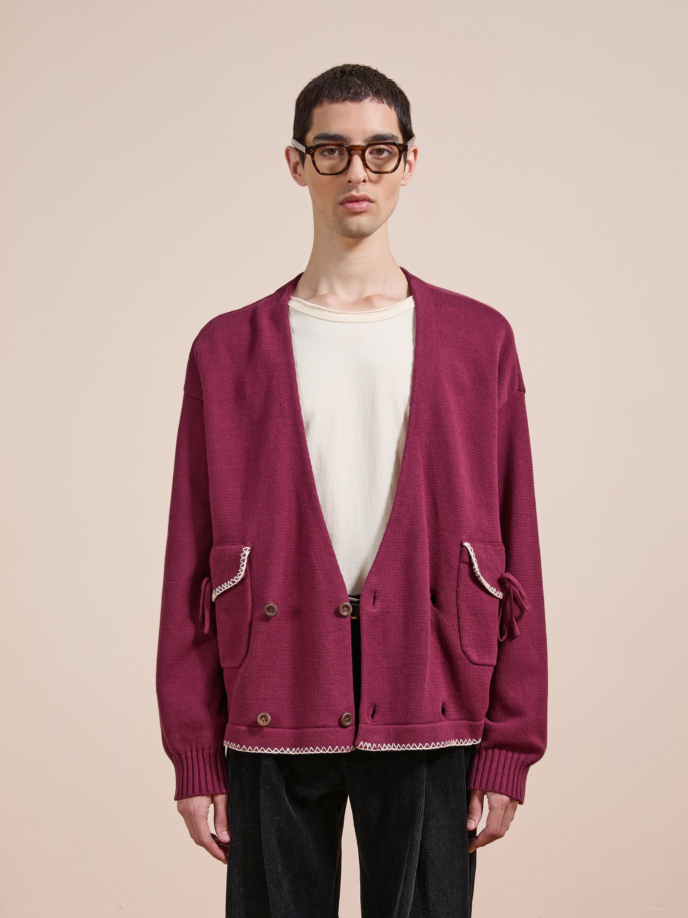 A person wearing glasses, a white t-shirt, and the FOUND Double Breasted Bow Cardigan stands against a plain beige background.