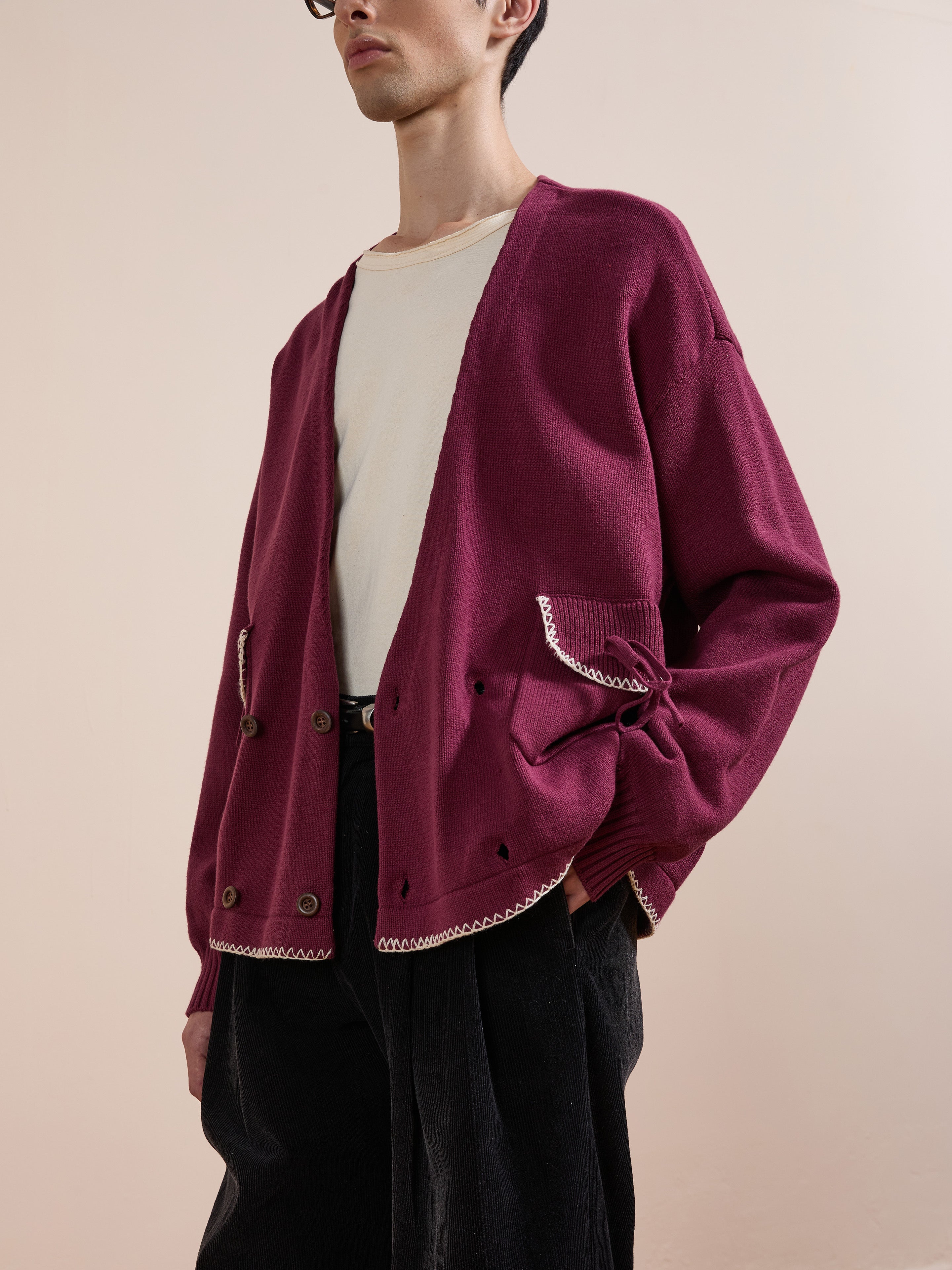 Wearing the FOUND Double Breasted Bow Cardigan in burgundy with white trim over a cream shirt and black pants, this person stands against a plain light background.