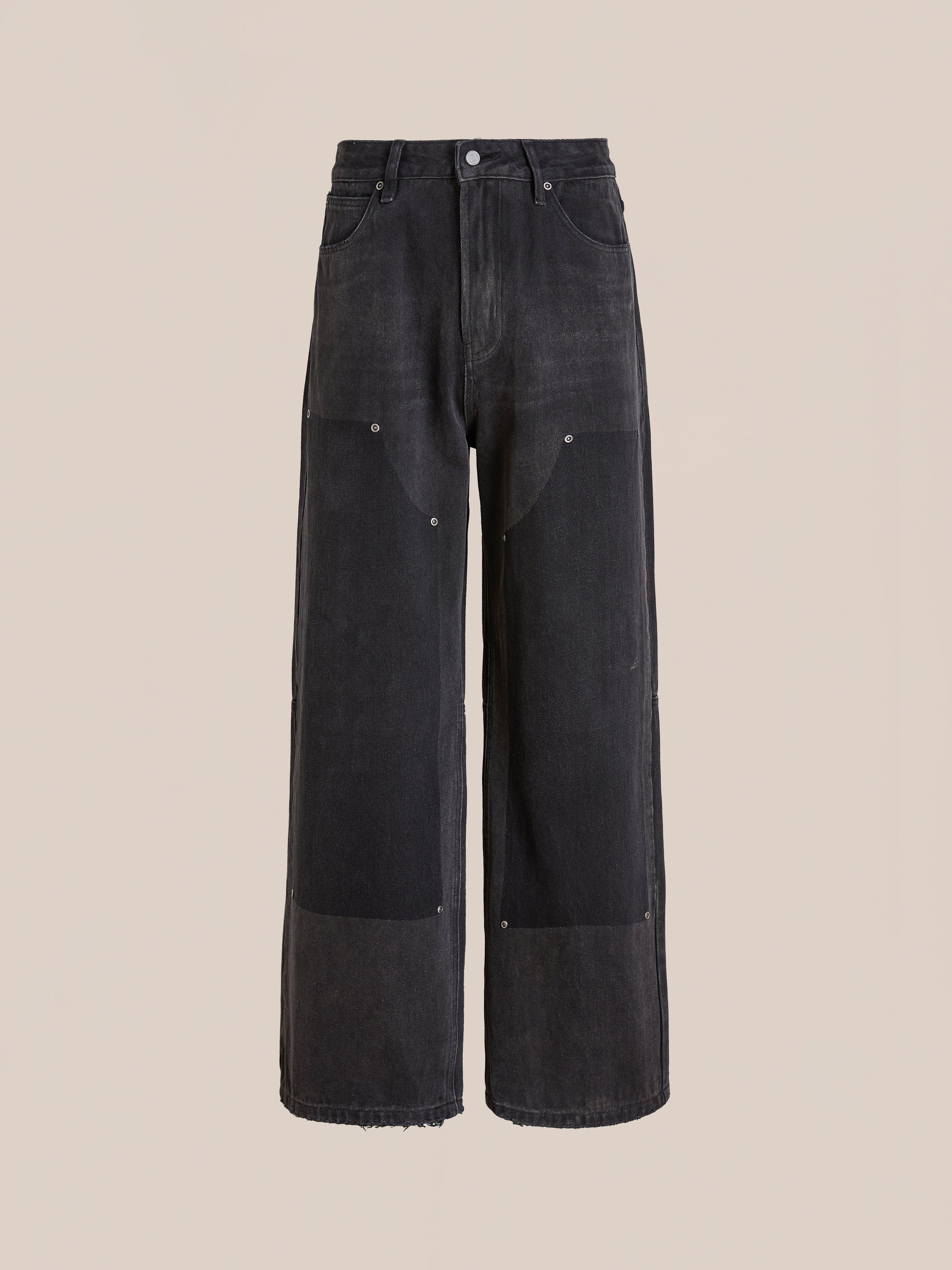 The FOUND Double Knee Carpenter Jeans feature a vintage black wash, patch details on the knees, front button and zip closure, and unfinished hems, shown against a plain beige background.