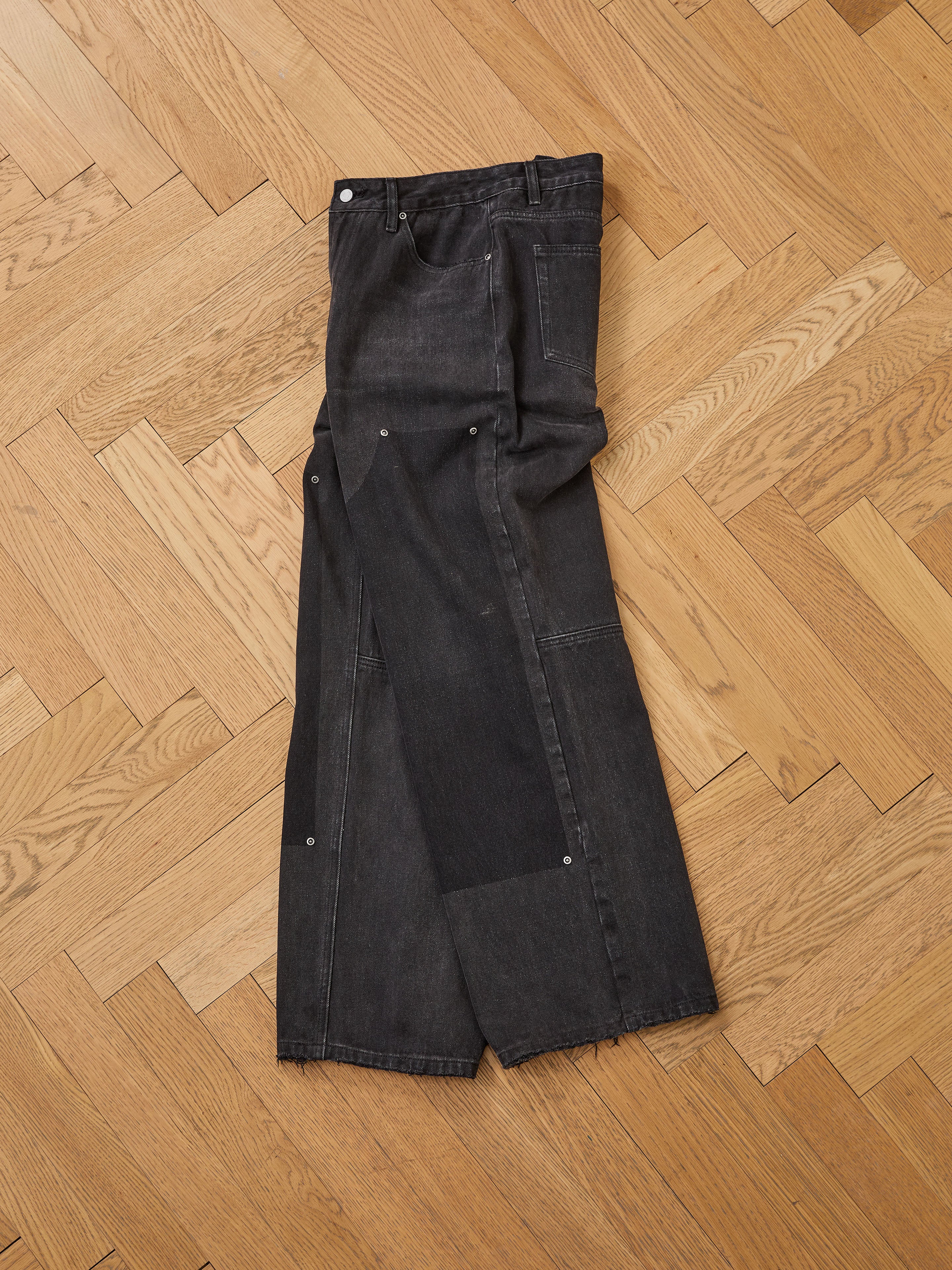 A pair of FOUND Double Knee Carpenter Jeans with relaxed fit, visible seam details, and raw hems is displayed flat on a wooden parquet floor.
