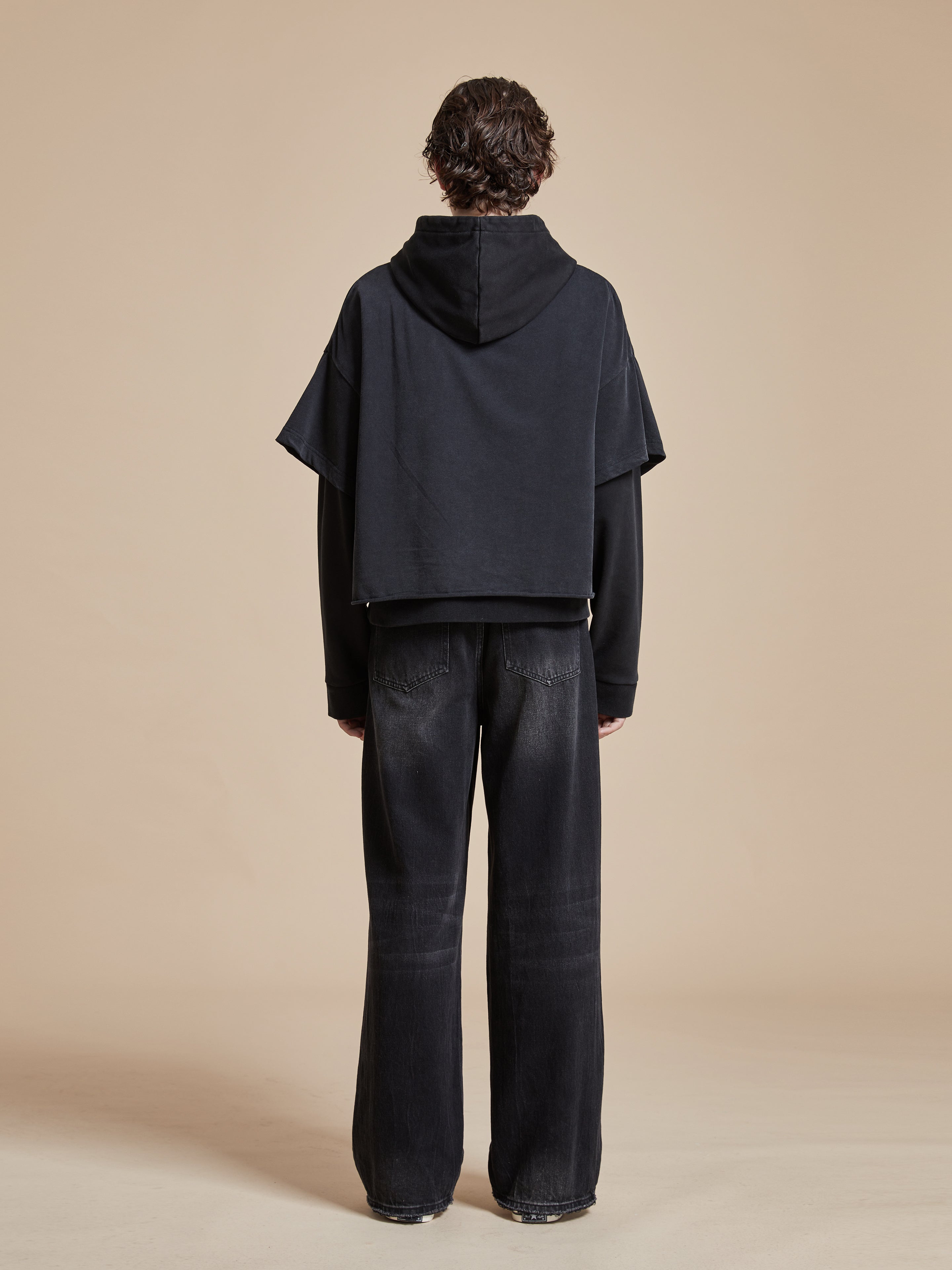 The back view of a man wearing a black Found Double Layer Hoodie and black pants, showcasing a pre-order item.