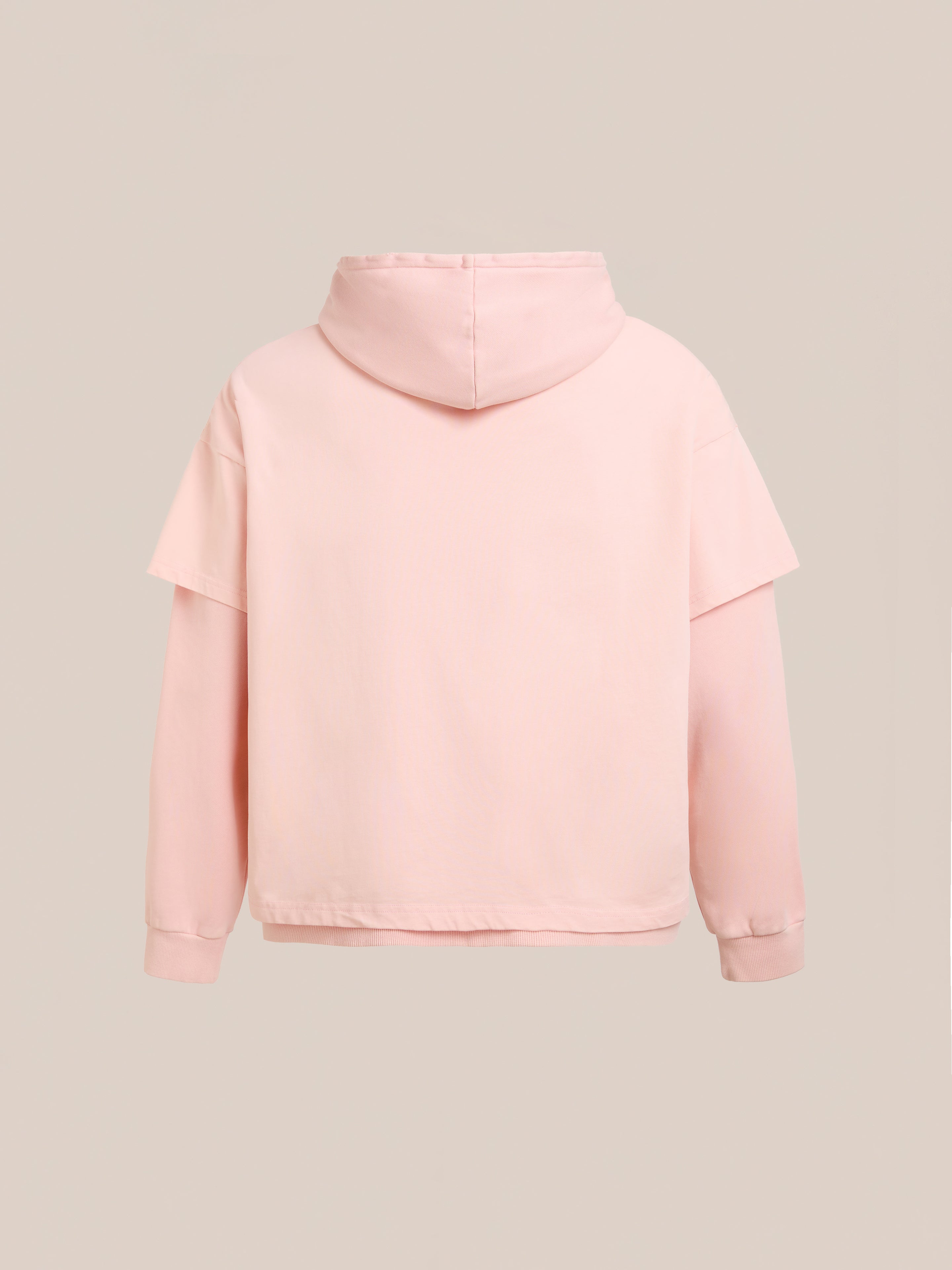 The Found Double Layer Hoodie in light pink French terry cotton, featuring a relaxed unisex fit, is displayed from the back against a plain beige background.