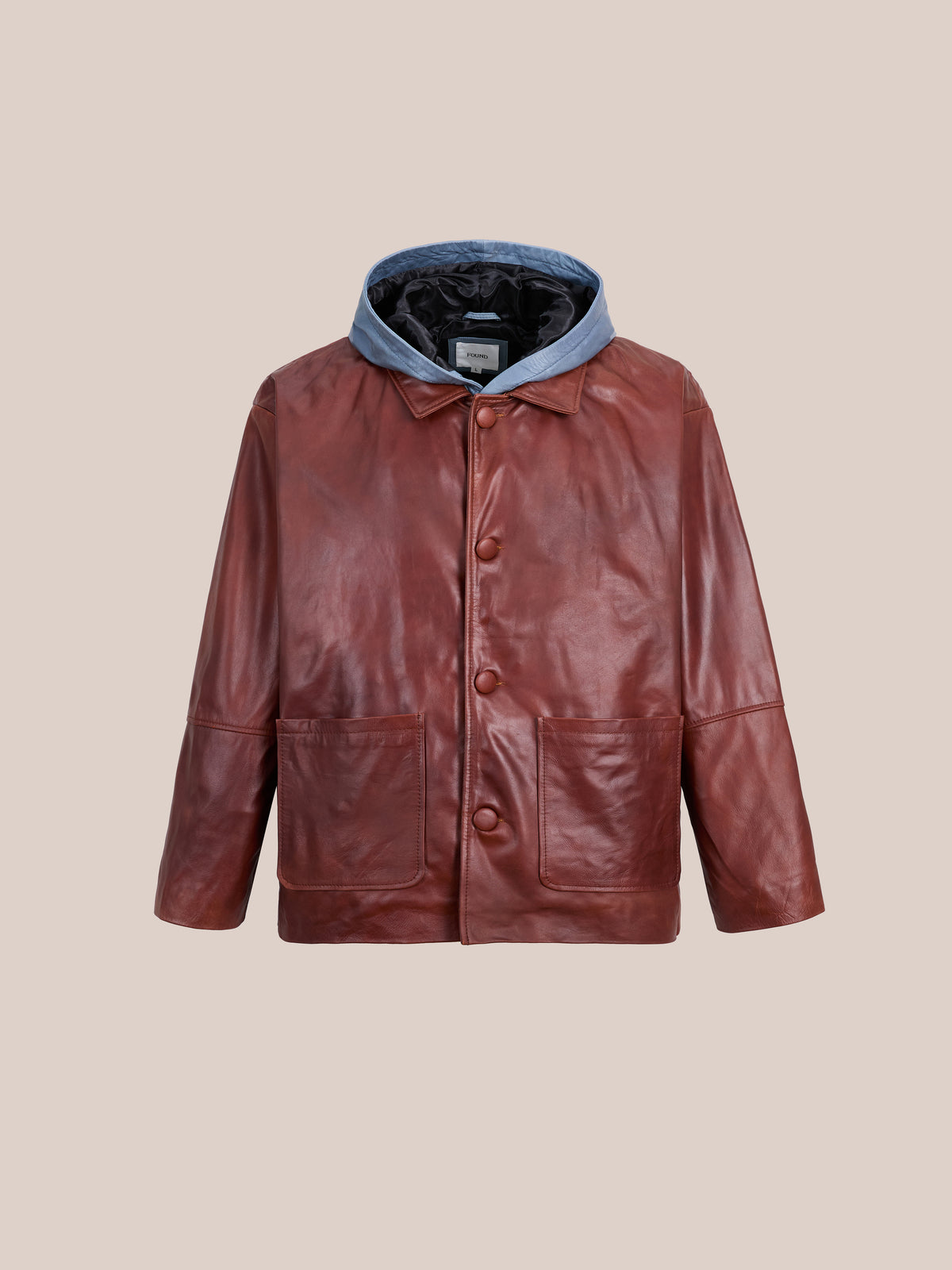 FOUND’s Double Layer Leather Hooded Jacket is a unisex brown leather jacket with large buttons, two front pockets, and a detachable gray hood. Showcased against a plain beige background, this piece features a double layer leather hoodie design for enhanced style and versatility.
