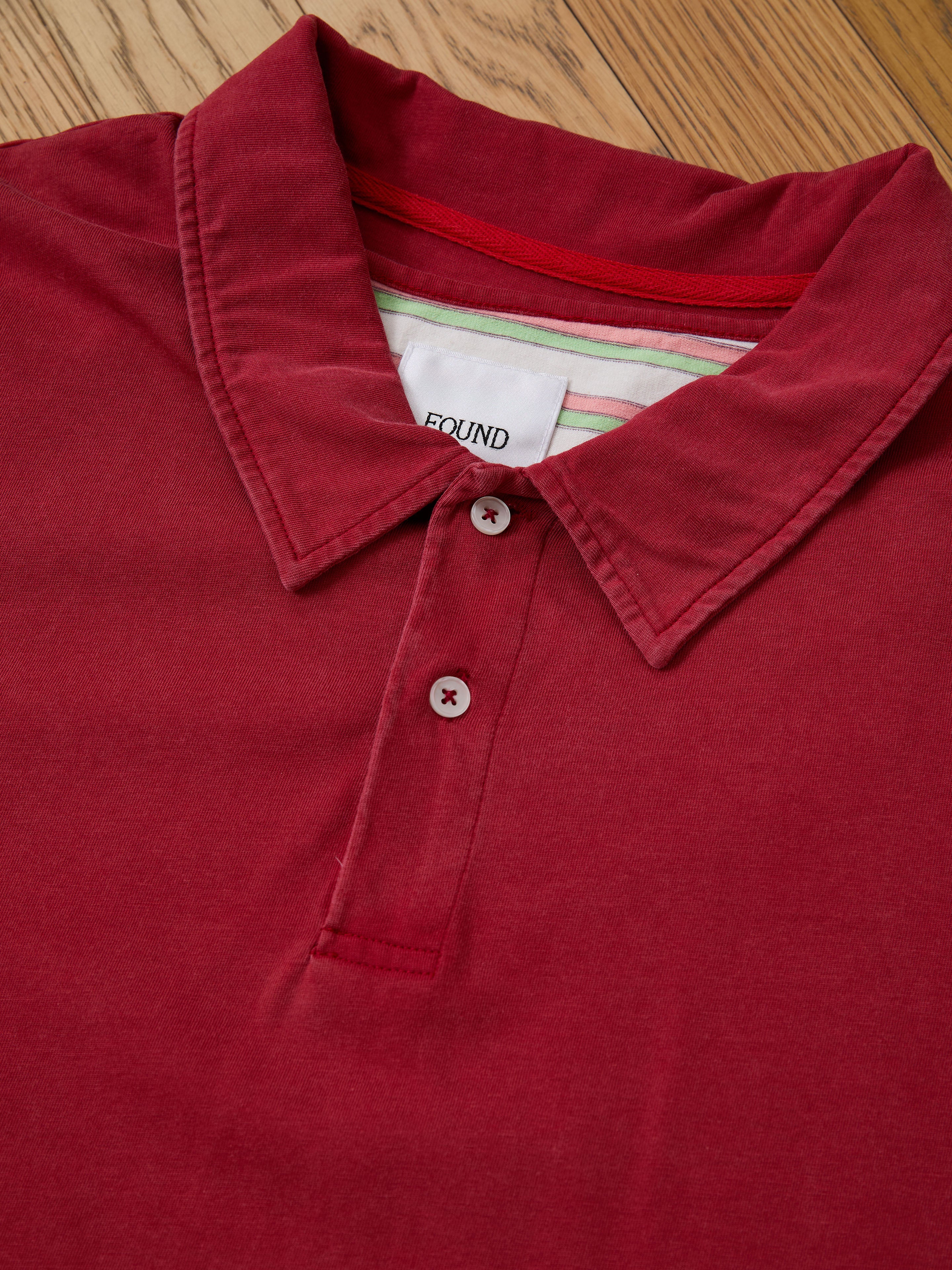 A FOUND Double Layer Stripe Polo in red with two buttons is displayed flat on wood. This unisex vintage athletic polo adds classic style to any sportswear collection.