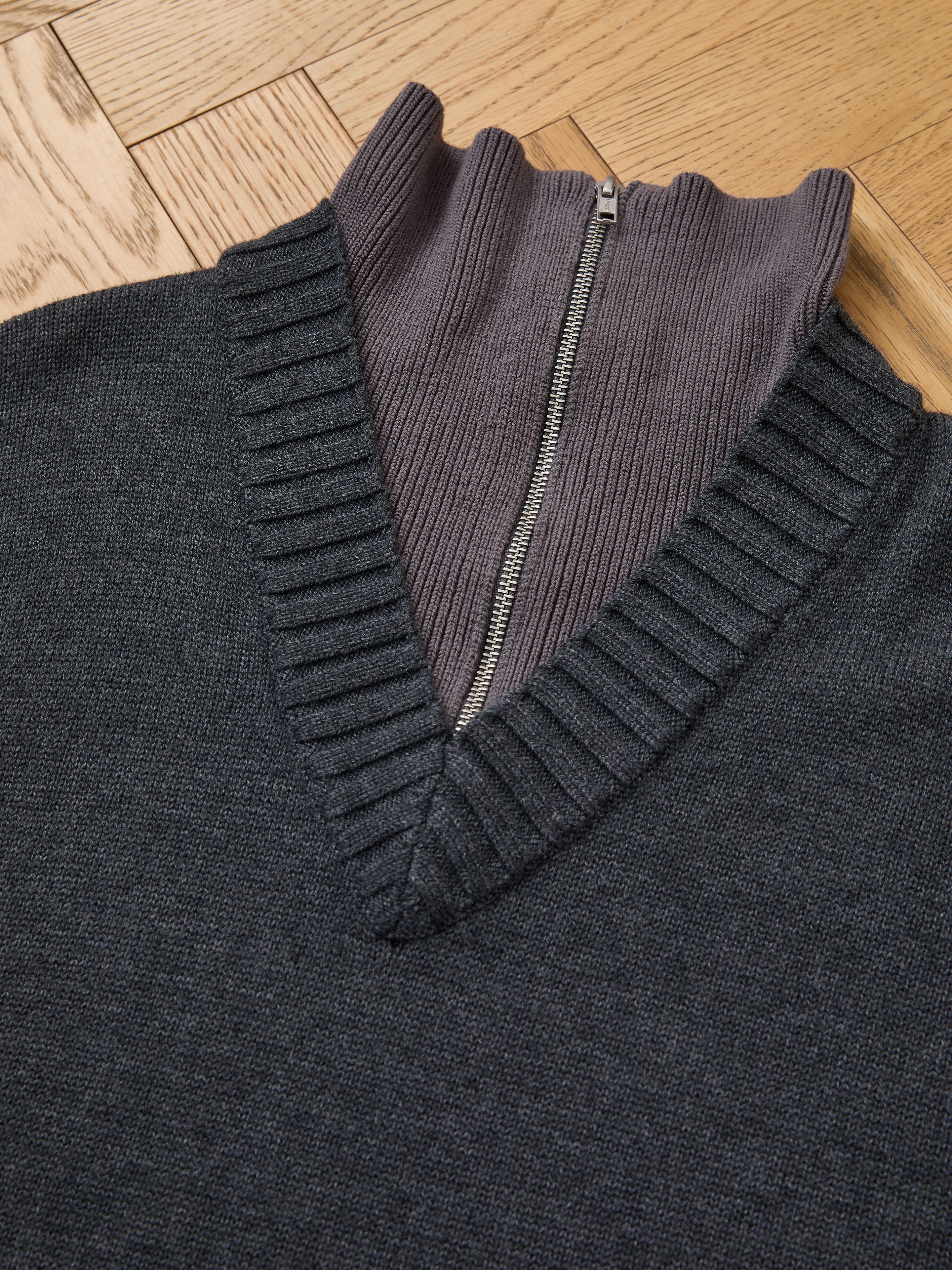 FOUND Double Layer Sweater: a dark grey wool blend V-neck layered over a ribbed zip-up mock neck, ideal for cold-weather layering, shown on a wooden floor.
